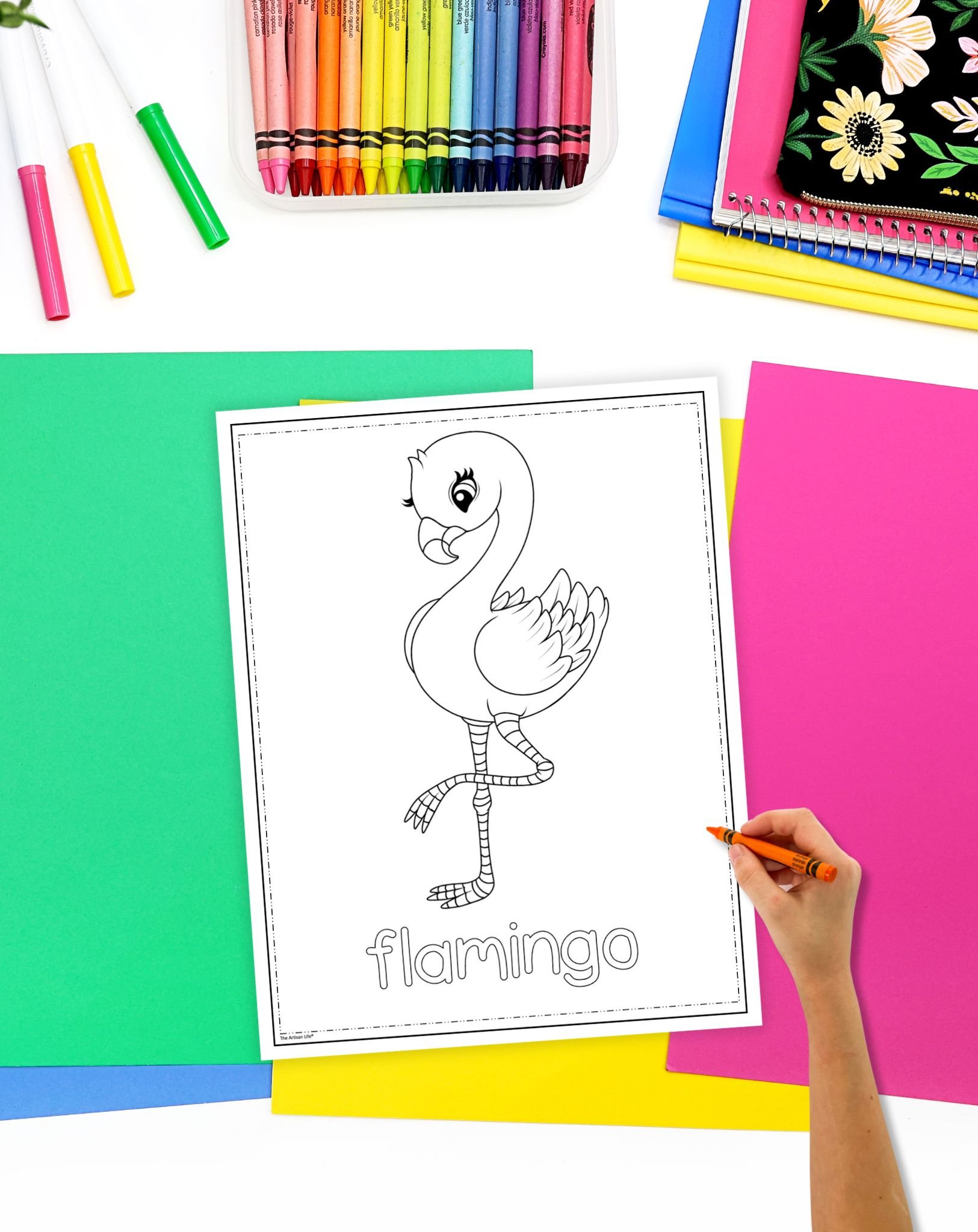a child's hand holding a crayon preparing to color a flamingo coloring page