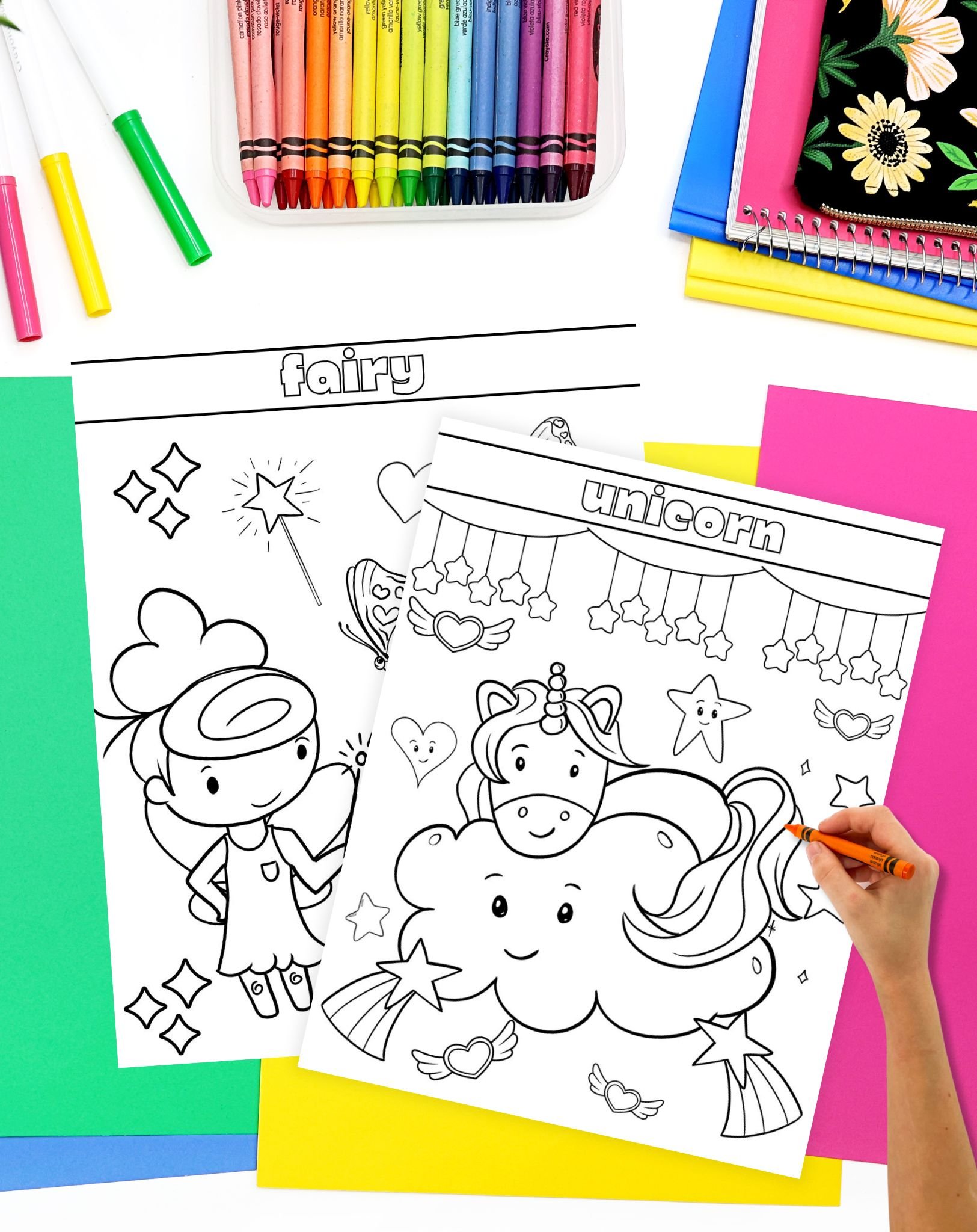 A child's hand colors an outline of a unicorn and a fairy on a coloring page, surrounded by colorful crayons and sheets of vibrant paper, suitable for fairy tale activities and princess coloring pages.
