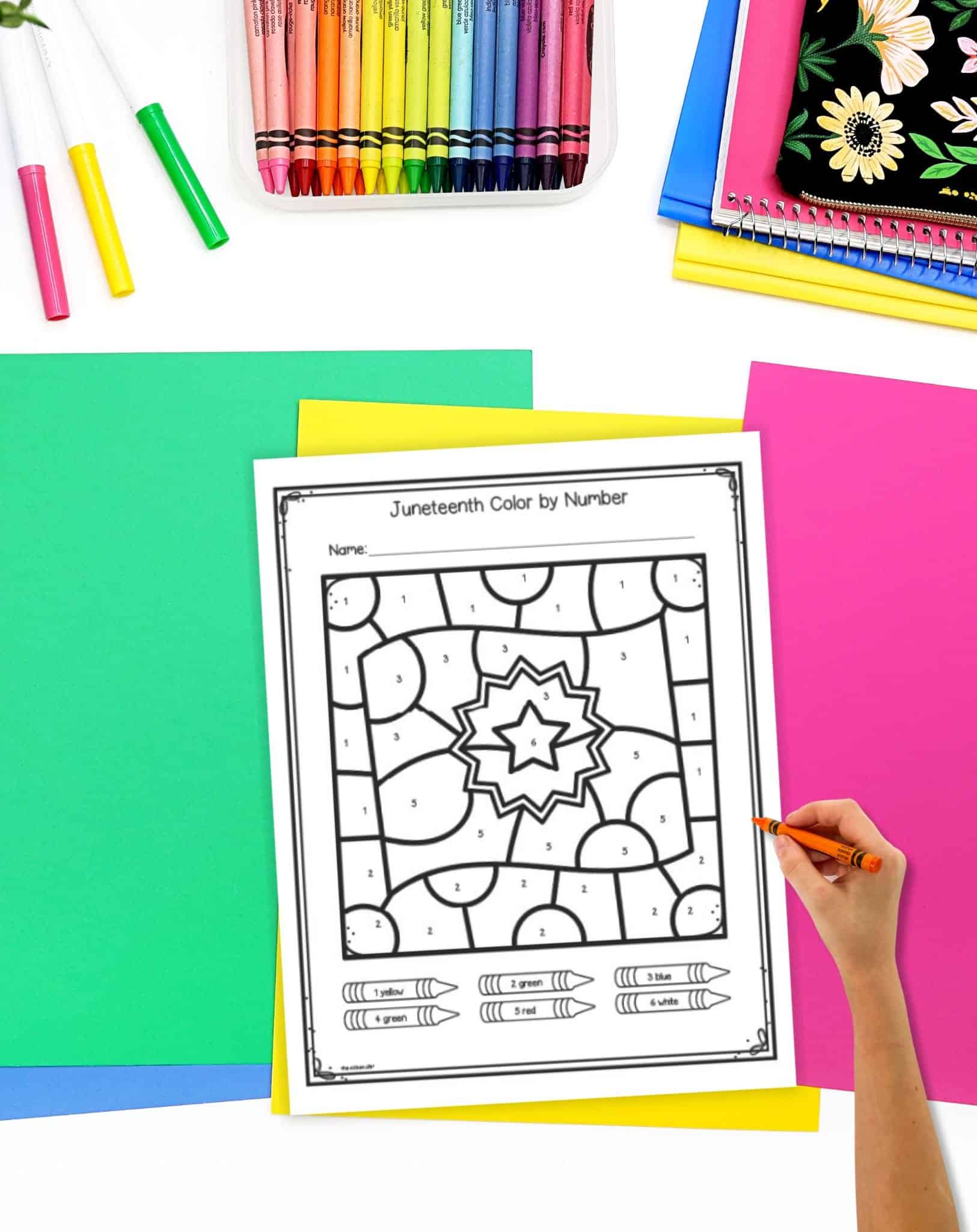 a hand with a crayon over a Juneteenth coloring page showing a flag