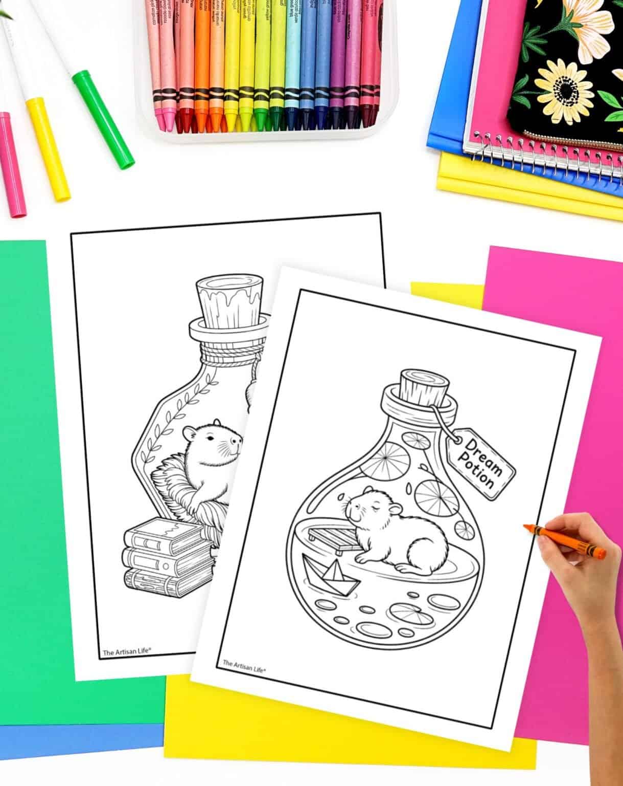 Two free printable capybara coloring pages are displayed on a colorful workspace, featuring a capybara inside a jar labeled "Dream Potion" and one resting on a stack of books.