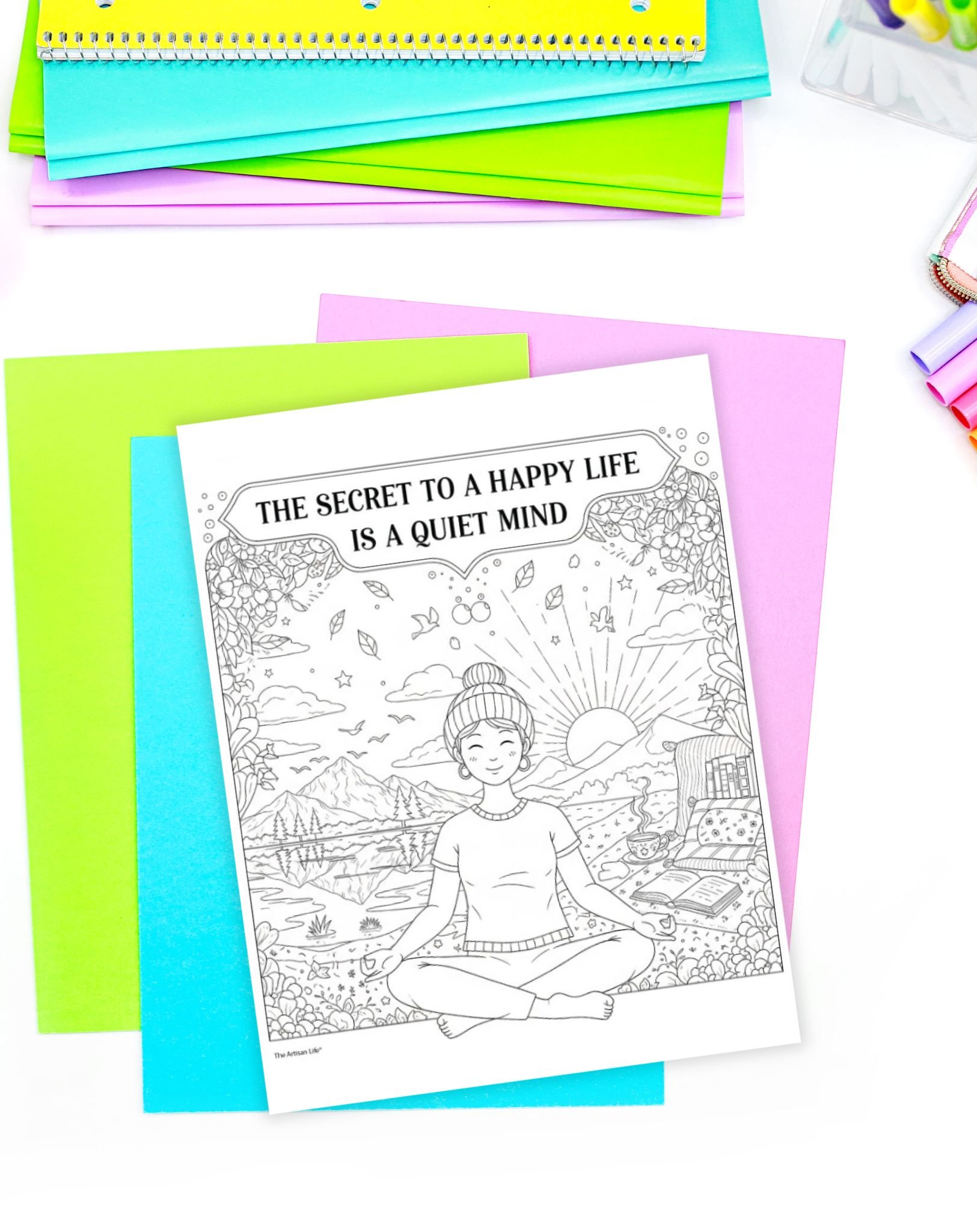 A coloring page titled "The Secret to a Happy Life is a Quiet Mind" featuring a meditating woman surrounded by nature, displayed among colorful sheets of paper.
