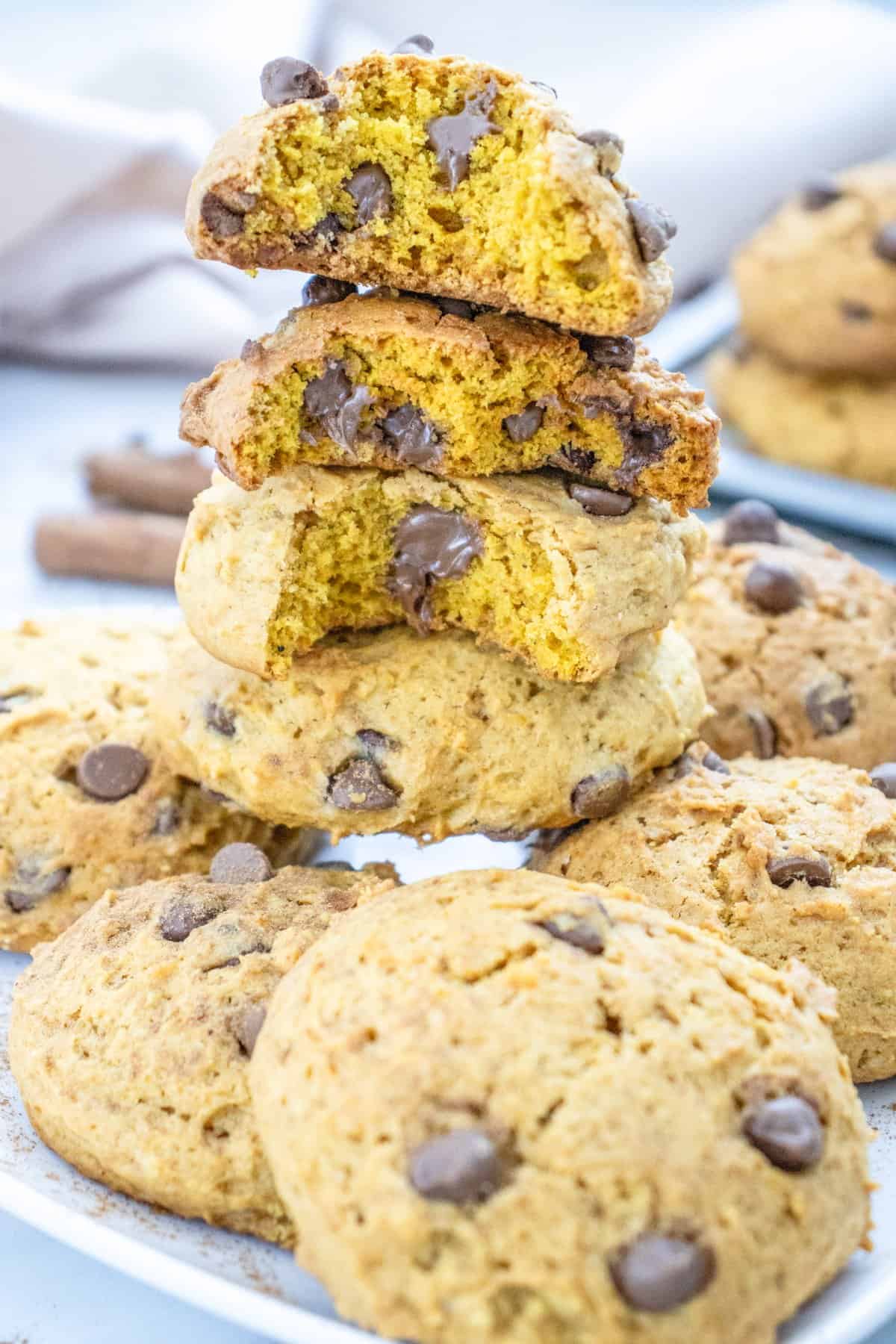 A stack of soft pumpkin cookies with chocolate chips, surrounded by cinnamon sticks, illustrating an easy pumpkin dessert recipe.

