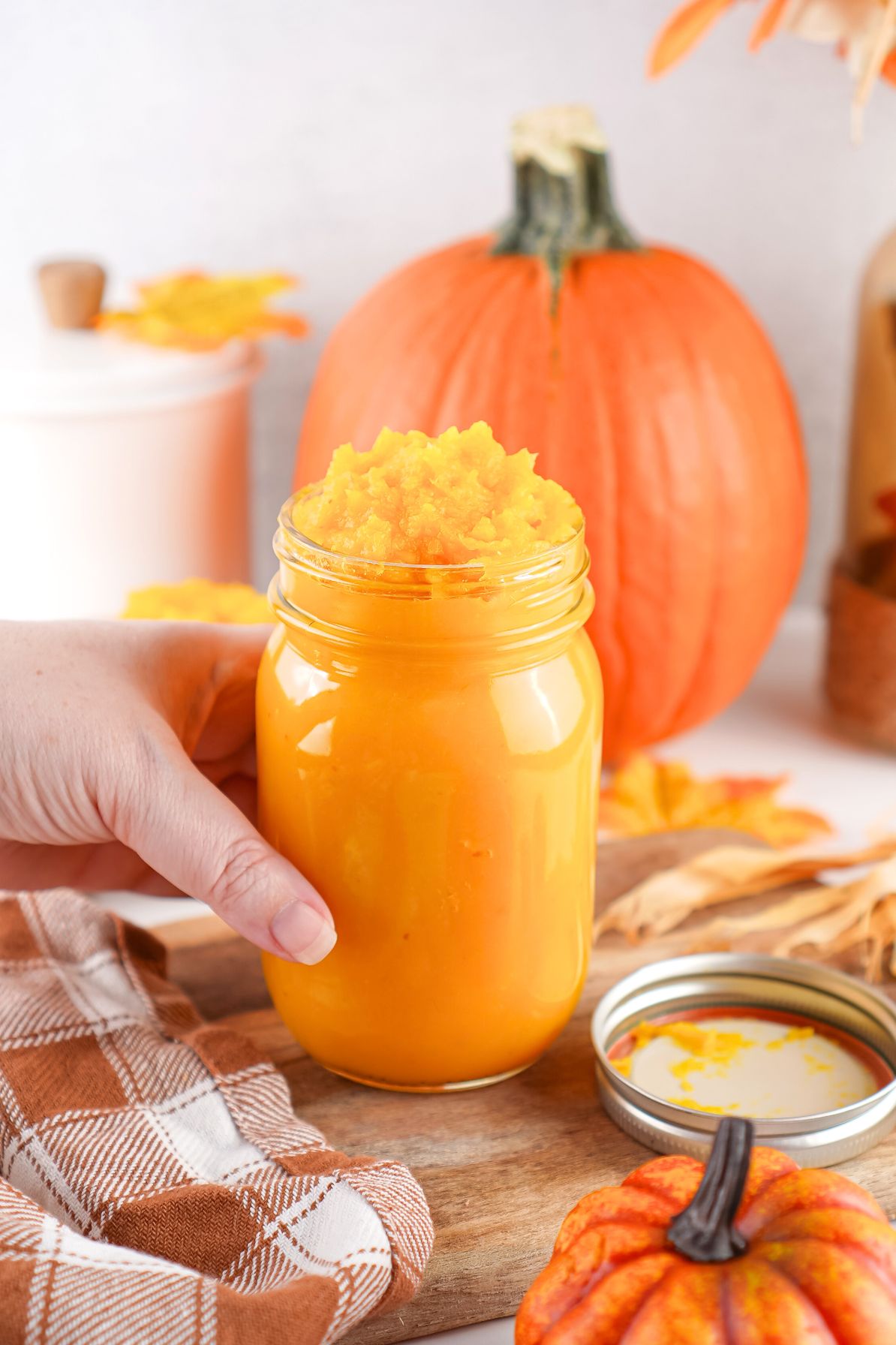 a hand holding a glass jar of homemade pumpkin puree