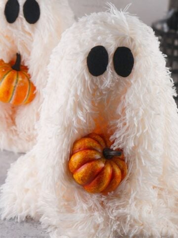 Two fluffy, white DIY ghosts, each holding a small orange pumpkin, are displayed as part of fall home decor, suitable for Halloween crafts.