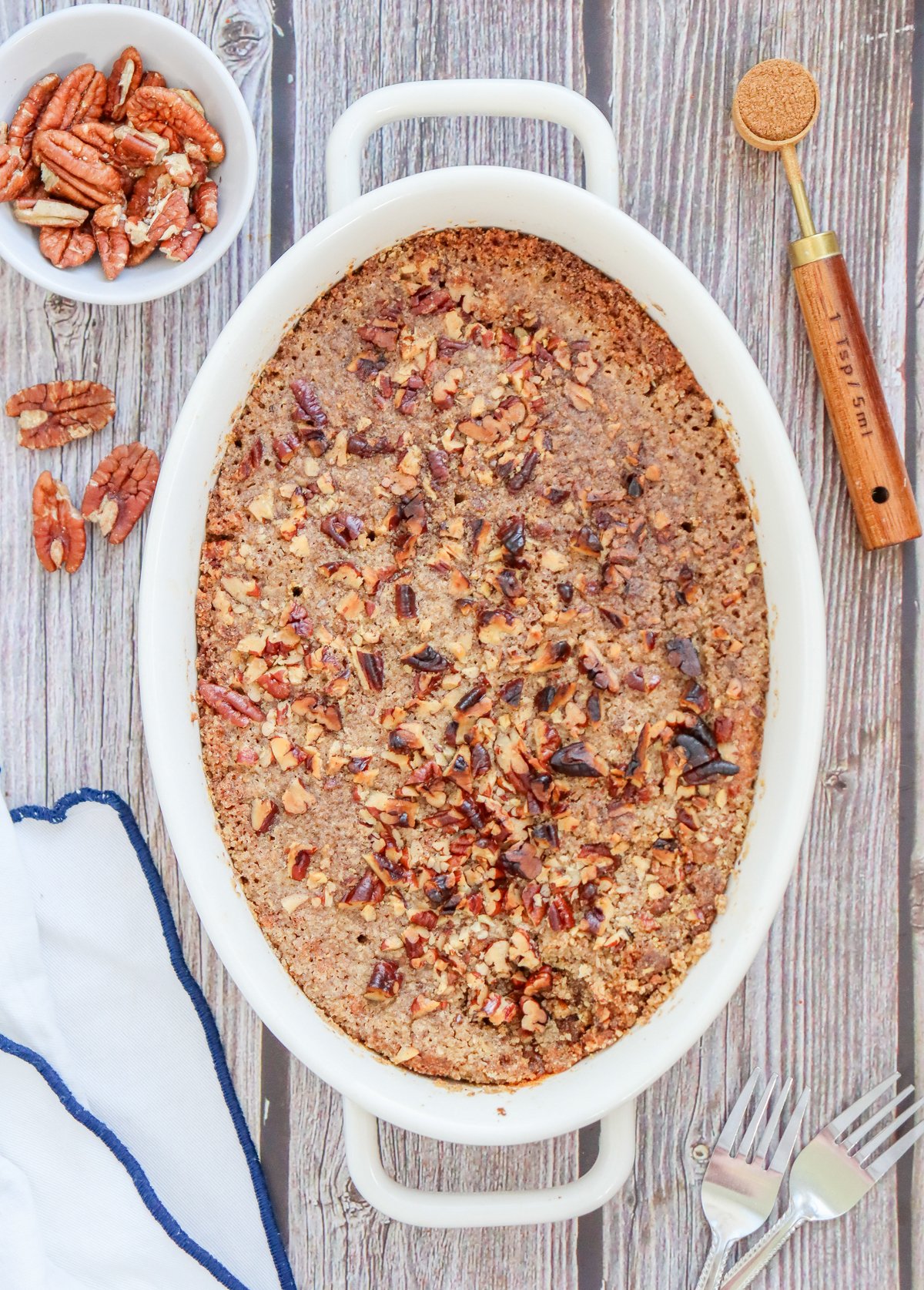 A gluten-free pumpkin dump cake topped with chopped pecans, presented in a white baking dish on a marble surface.
