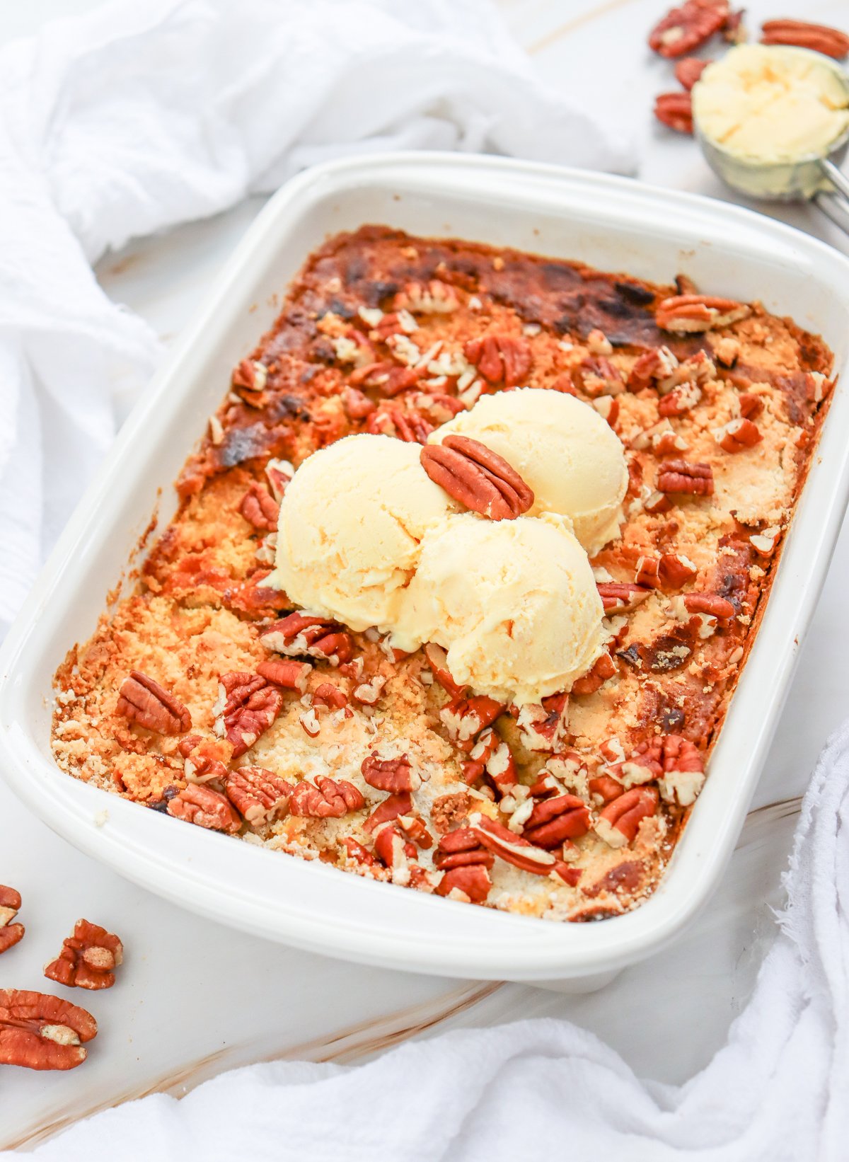 A freshly baked pumpkin dump cake topped with three scoops of vanilla ice cream and sprinkled with pecans, showcasing an easy pumpkin dessert recipe.
