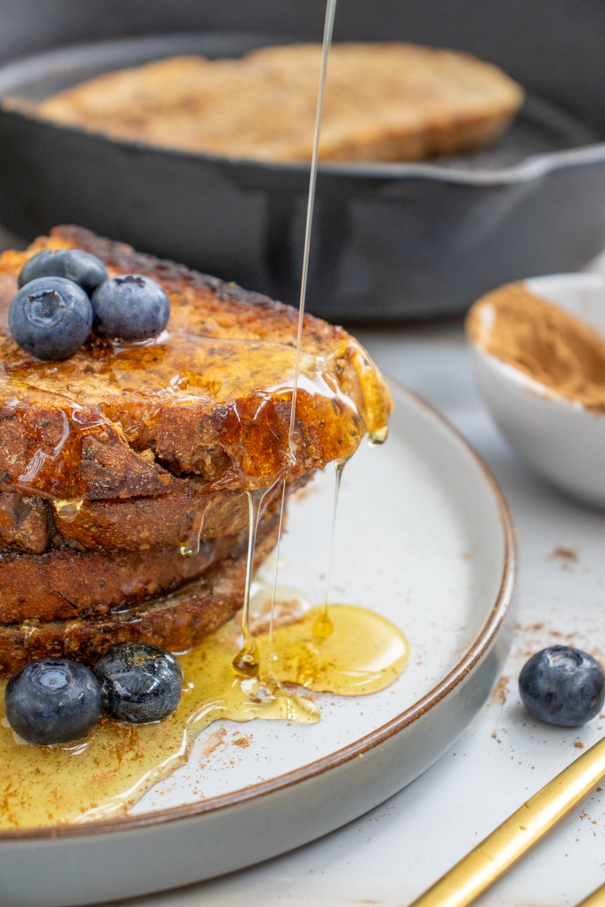 A stack of sourdough toast drizzled with honey sits on a plate with a small bowl of cinnamon in the background, suggesting sweet sourdough toast ideas for breakfast.

