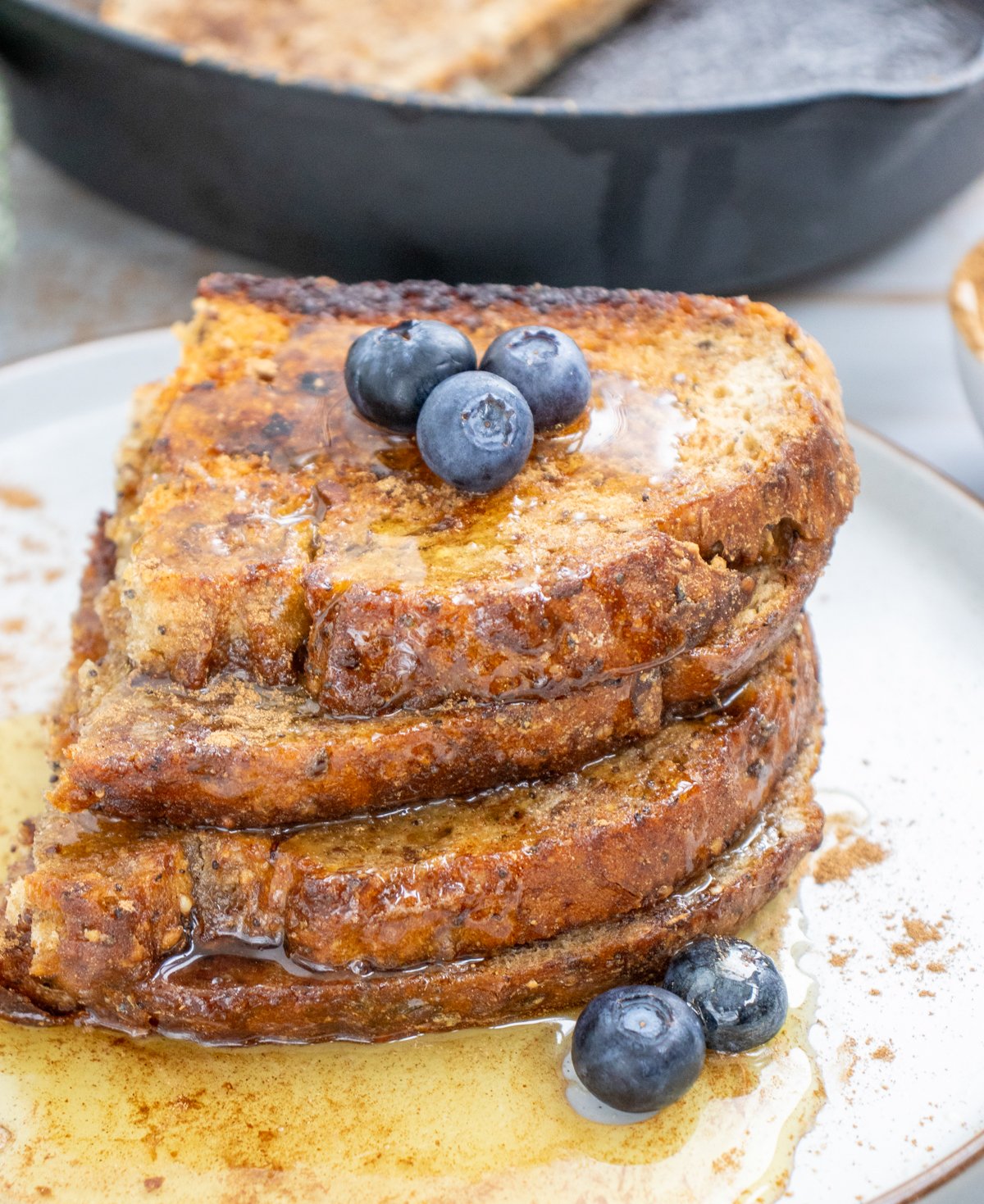 A stack of sourdough toast drizzled with honey sits on a plate with a small bowl of cinnamon in the background, suggesting sweet sourdough toast ideas for breakfast.
