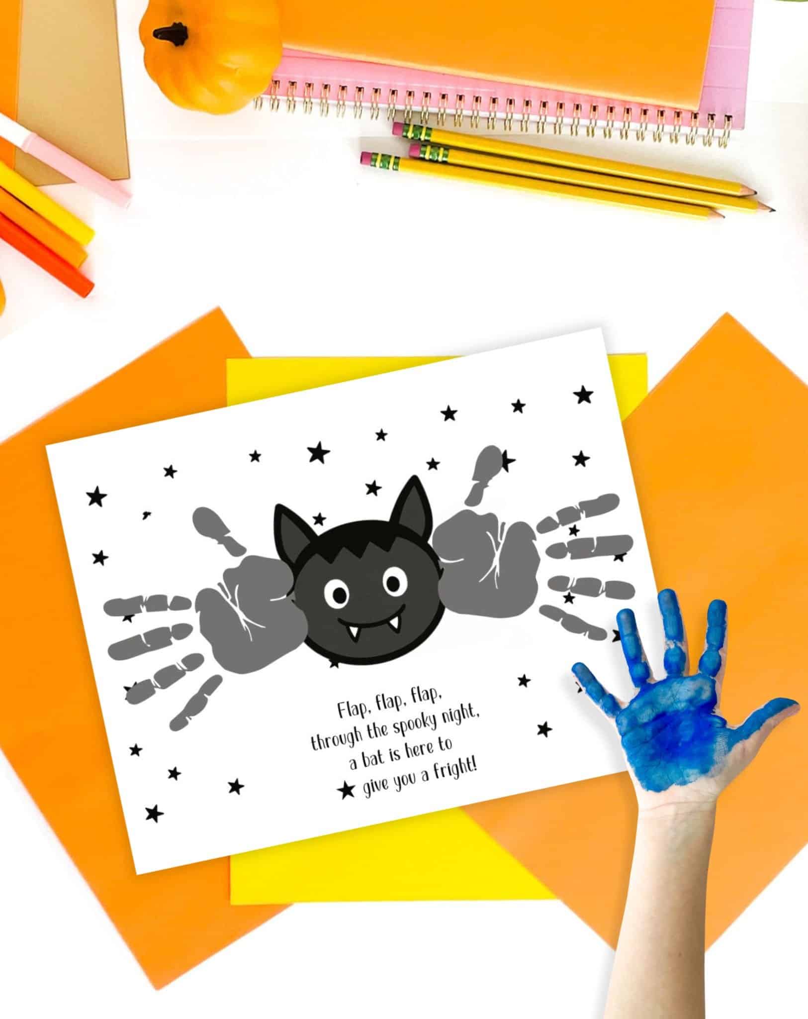 A colorful handprint with blue paint is placed next to a Halloween-themed printable art template featuring a bat and surrounding handprints, accompanied by text that reads, "Flap, flap, flap, through the spooky night, a bat is here to give you a fright!"
