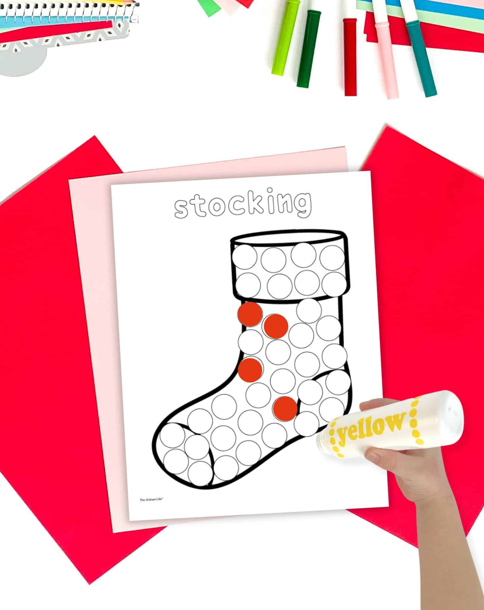 a hand with a dot marker coloring a Christmas dot painting page showing a Christmas stocking