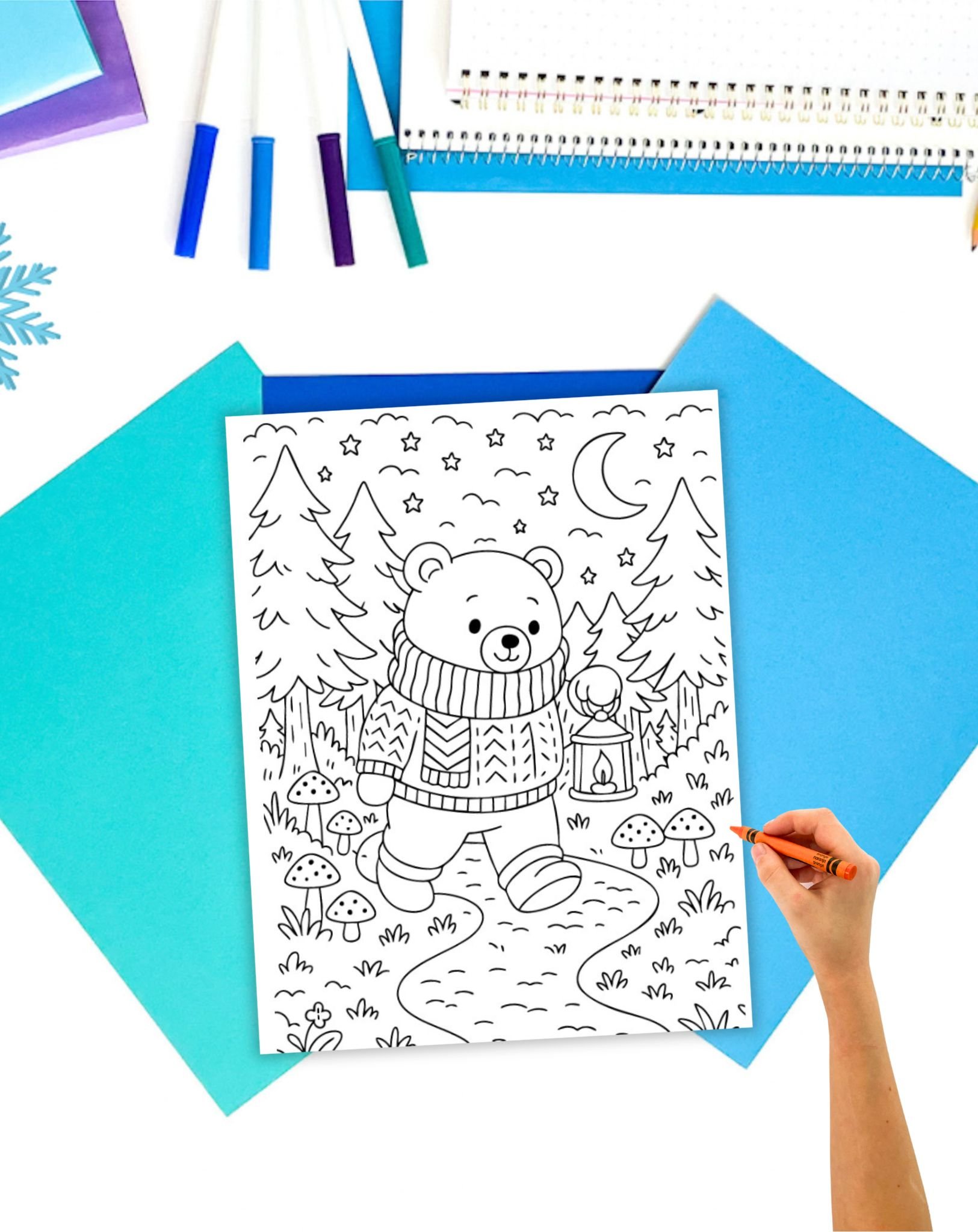 a hand with an orange crayon coloring a coloring page showing a bear in a sweater holding a lantern