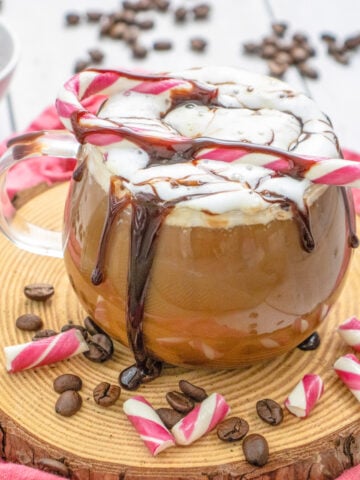a peppermint mocha in a glass mug with a candy cane on top