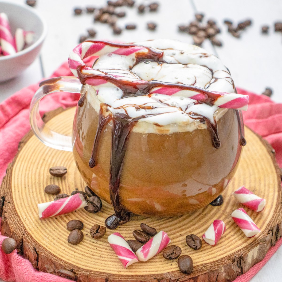 a peppermint mocha in a glass mug with a candy cane on top