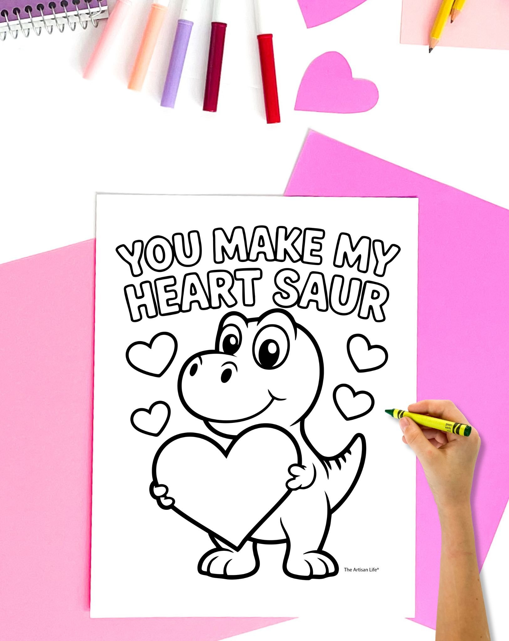 a hand holding a green crayon preparing to color a dinosaur Valentine's Day coloring page