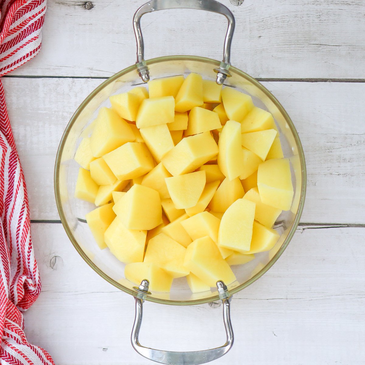 A glass bowl contains chopped yellow potatoes, which are ready to be used in mashed potato recipes, including creamy garlic mashed potatoes and herb mashed potatoes for Christmas dinner side dishes.