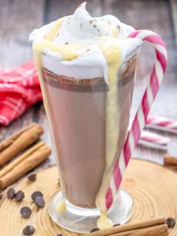 a glass mug with hot chocolate egg nog served with whipped cream and a candy cane