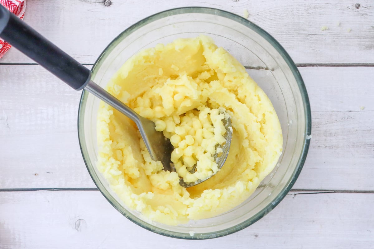 A glass bowl contains creamy mashed potatoes, surrounded by a red and white striped kitchen towel, suggesting a homemade dish ideal for Christmas dinner side dishes.