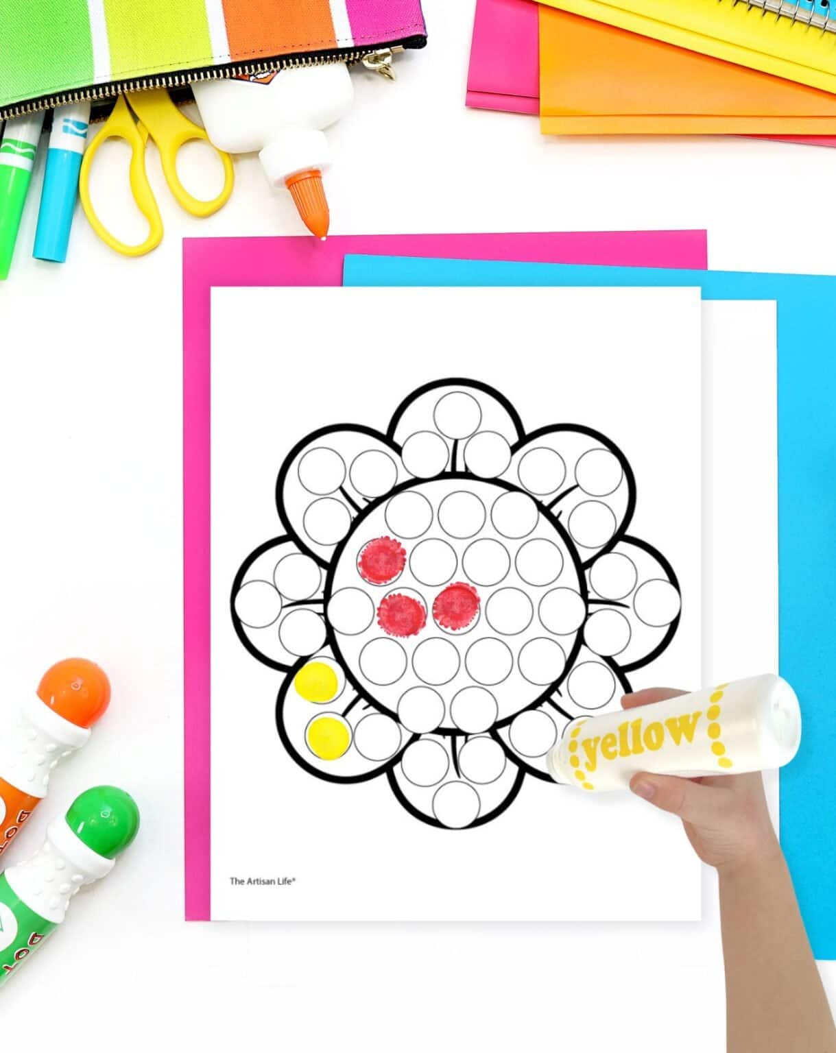a child's hand with a yellow marker coloring a daisy dot marker coloring page
