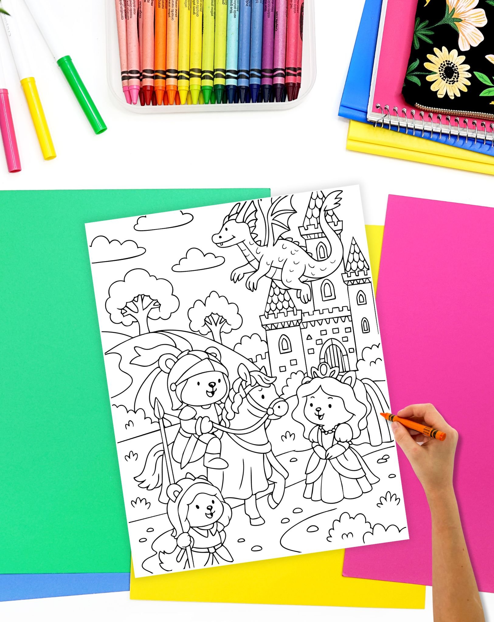 A hand with an orange crayon coloring a coloring sheet showing animals dressed as knights and a princess outside of a castle