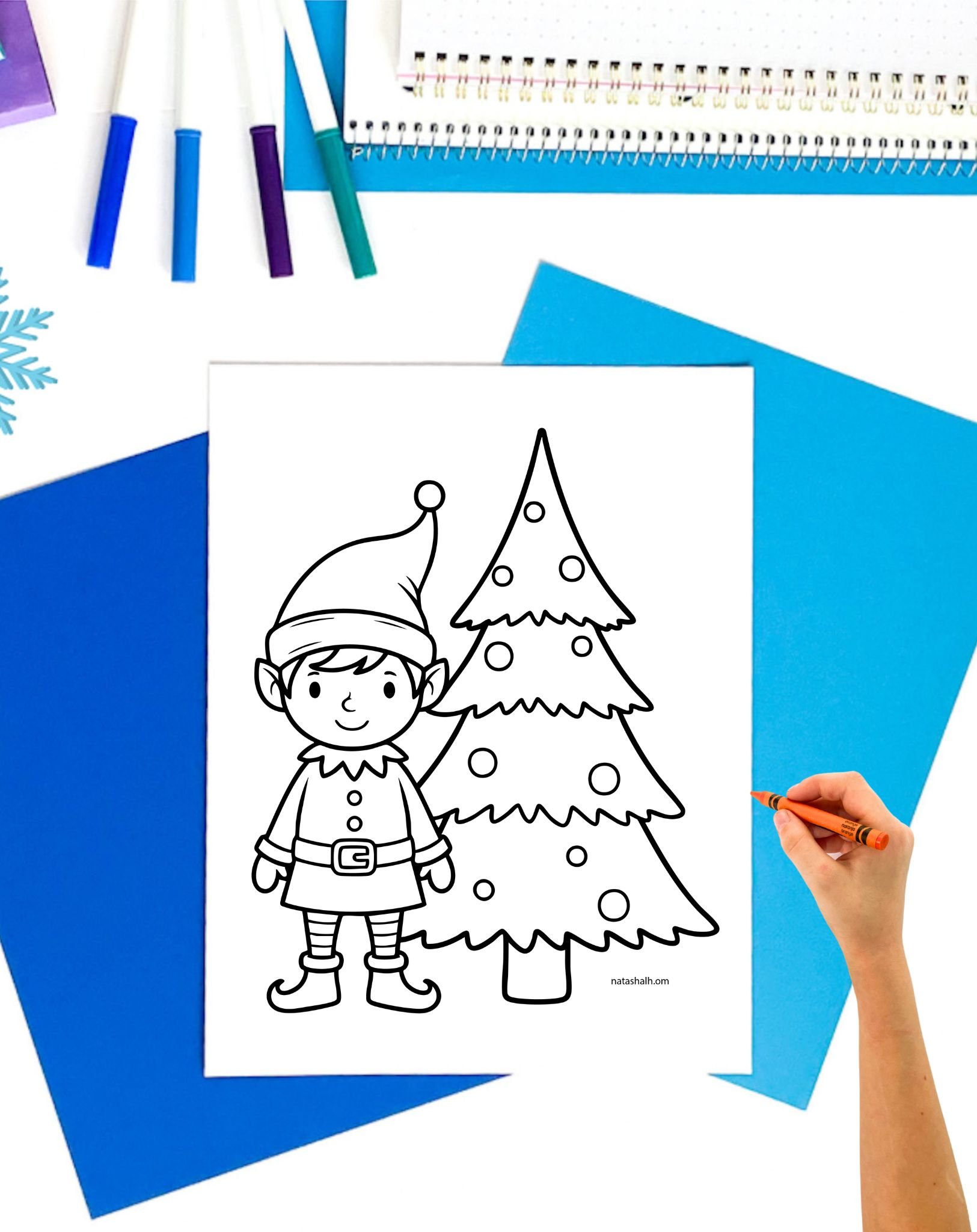 a hand with an orange crayon preparing to color an easy christmas coloring page showing an elf near a tree
