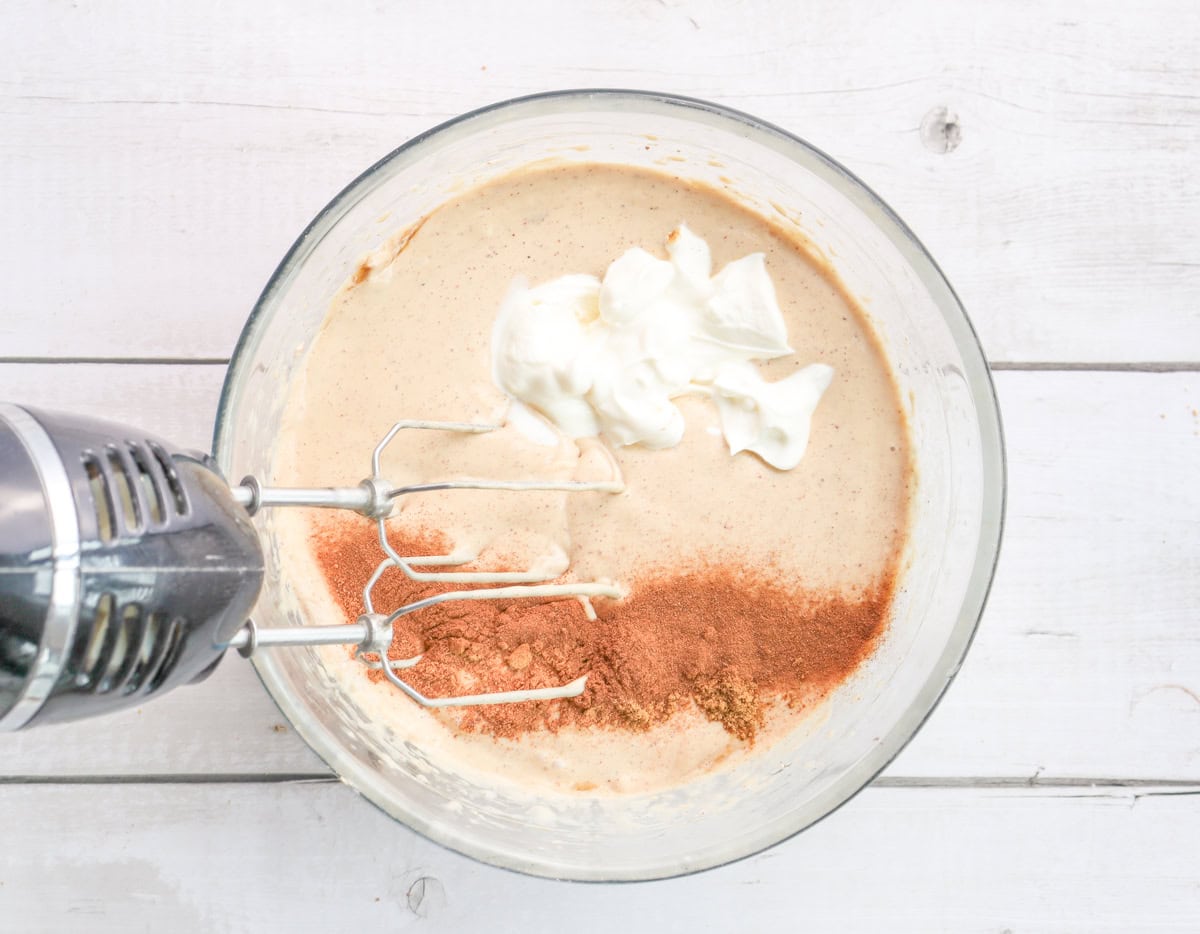 A mixing bowl contains a blend of cream cheese, brown sugar, and spices