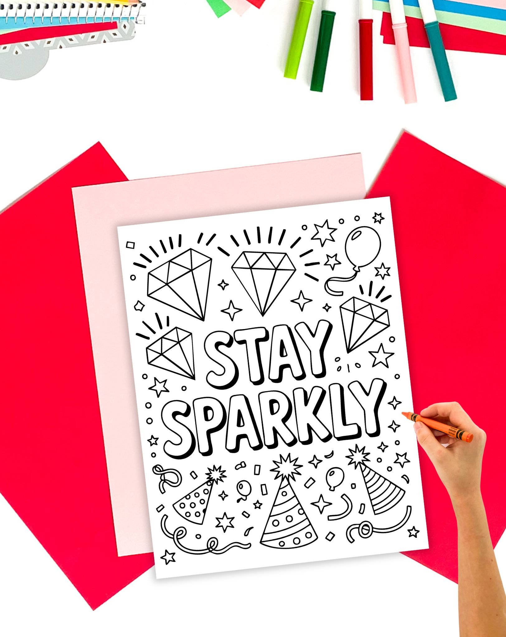a child's hand with an orange crayon coloring a new Year's coloring page with the message to "stay sparkly"