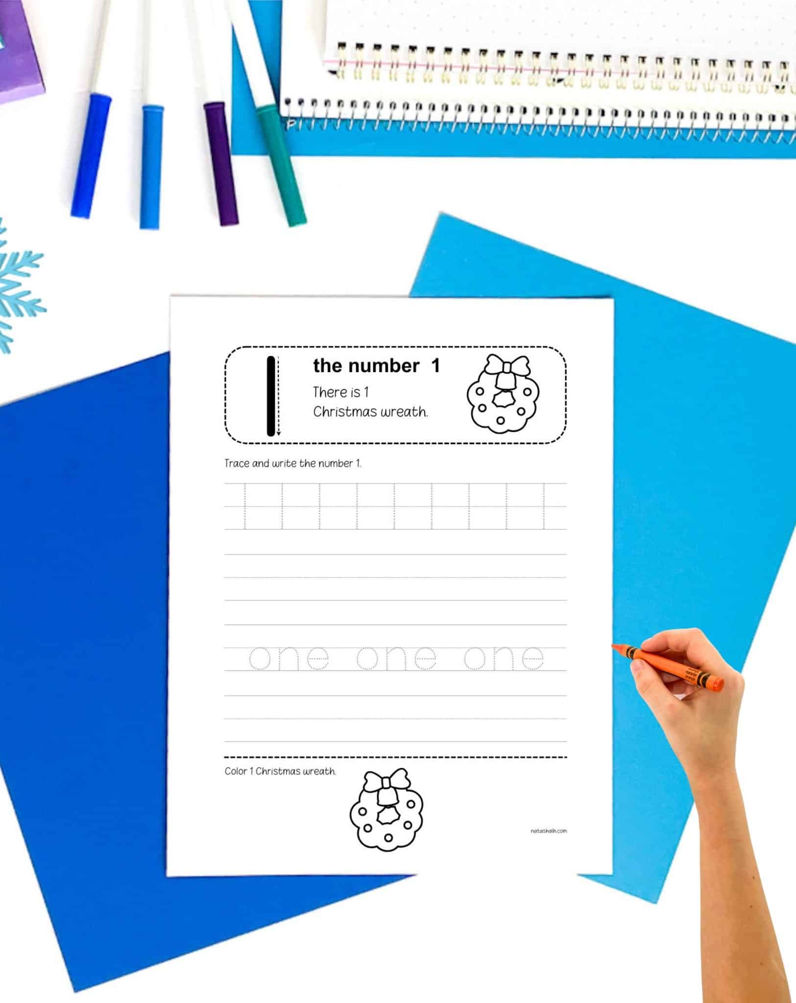 a chid's hand holding a crayon preparing to use a number one tracing page with a Christmas theme