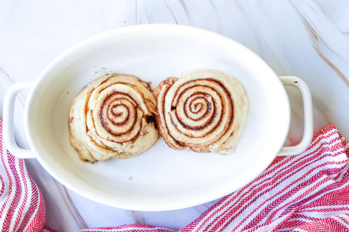 A close-up of two raw easy small batch cinnamon rolls on a wooden surface, showcasing the spiral design and cinnamon filling, ideal for a homemade treats recipe, including instructions on how to make cinnamon rolls in 1 hour for Valentine's Day.