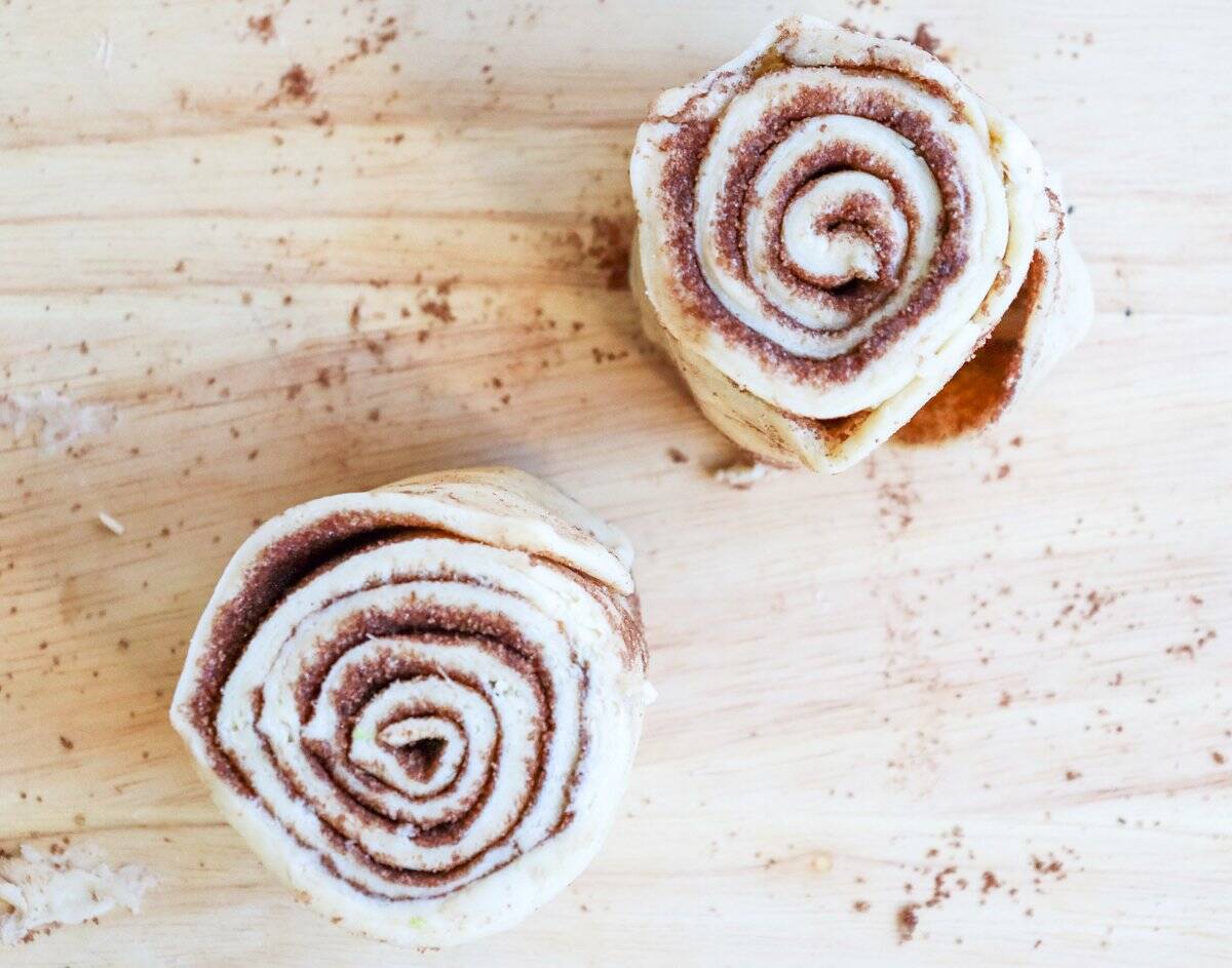 Two unbaked cinnamon roll pieces are shown on a wooden surface, illustrating the process of making easy small batch cinnamon rolls, suitable for Valentine's Day and other homemade treats.