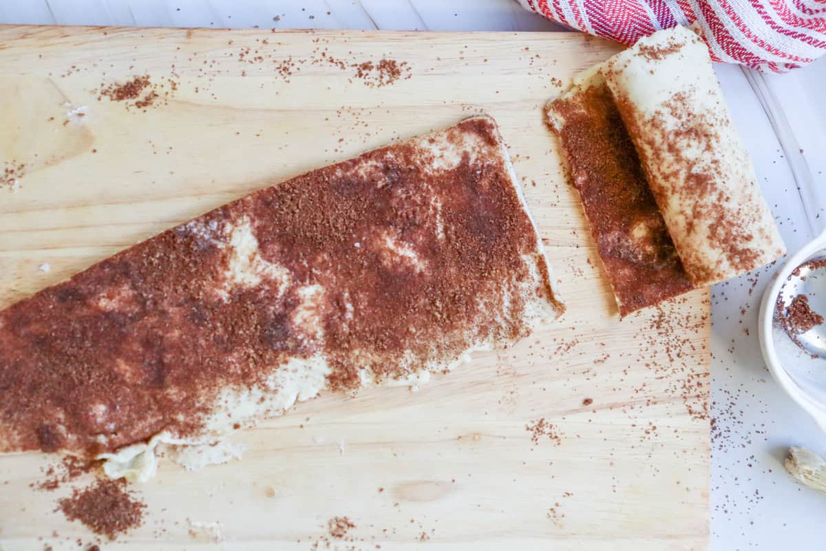 An uncooked rolled dough spread with cinnamon and sugar sits on a wooden surface, showcasing the preparation of easy small batch cinnamon rolls for a homemade treat.