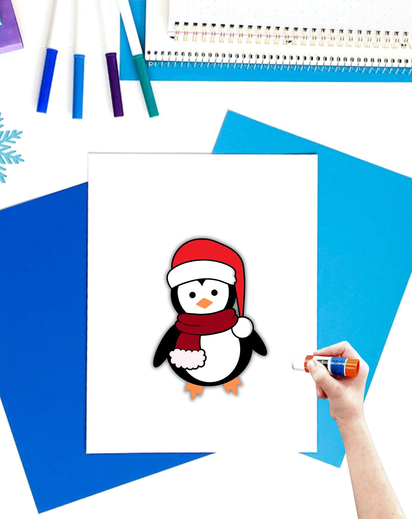 a completed build a penguin craft with a child's hadn't holding a glue stick