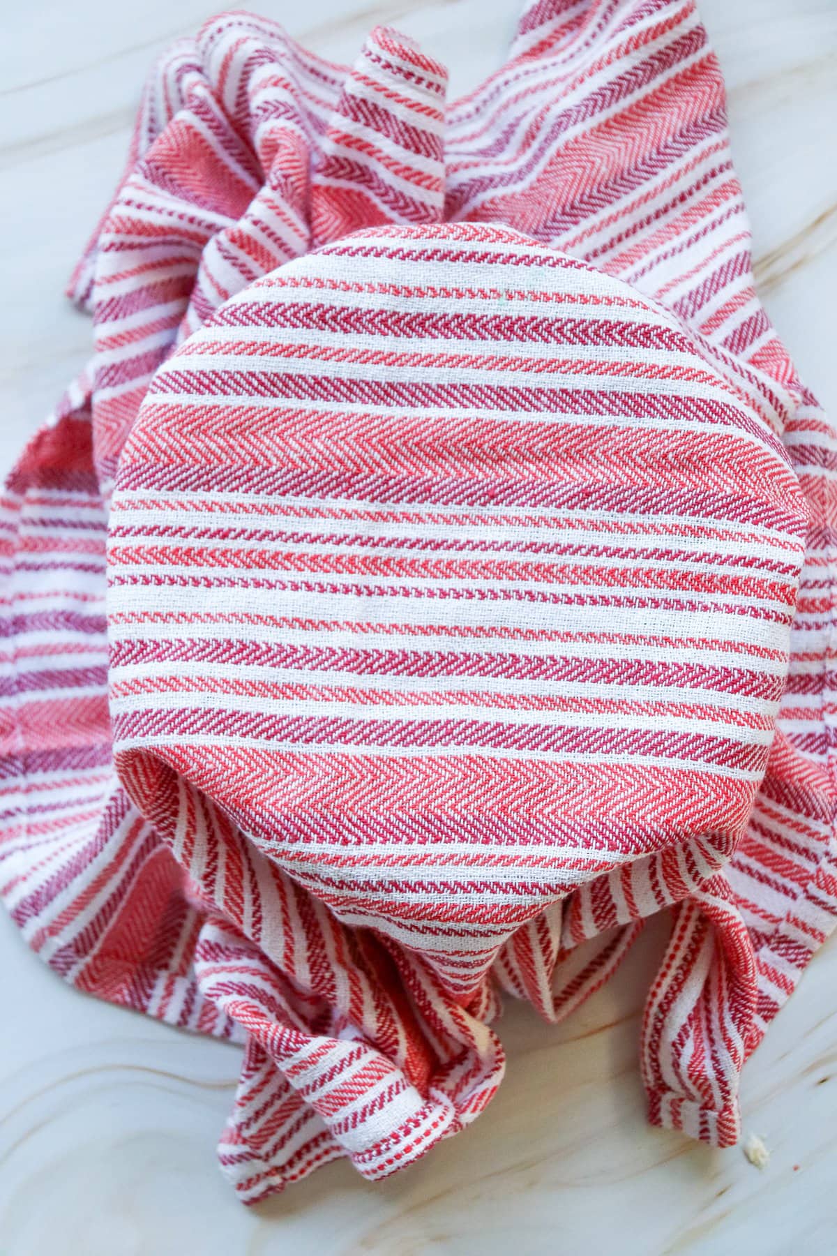 A red and white striped towel covers a bowl on a countertop, possibly containing dough for easy small batch cinnamon rolls, which can be made in one hour for homemade treats like Valentine's Day cinnamon rolls.