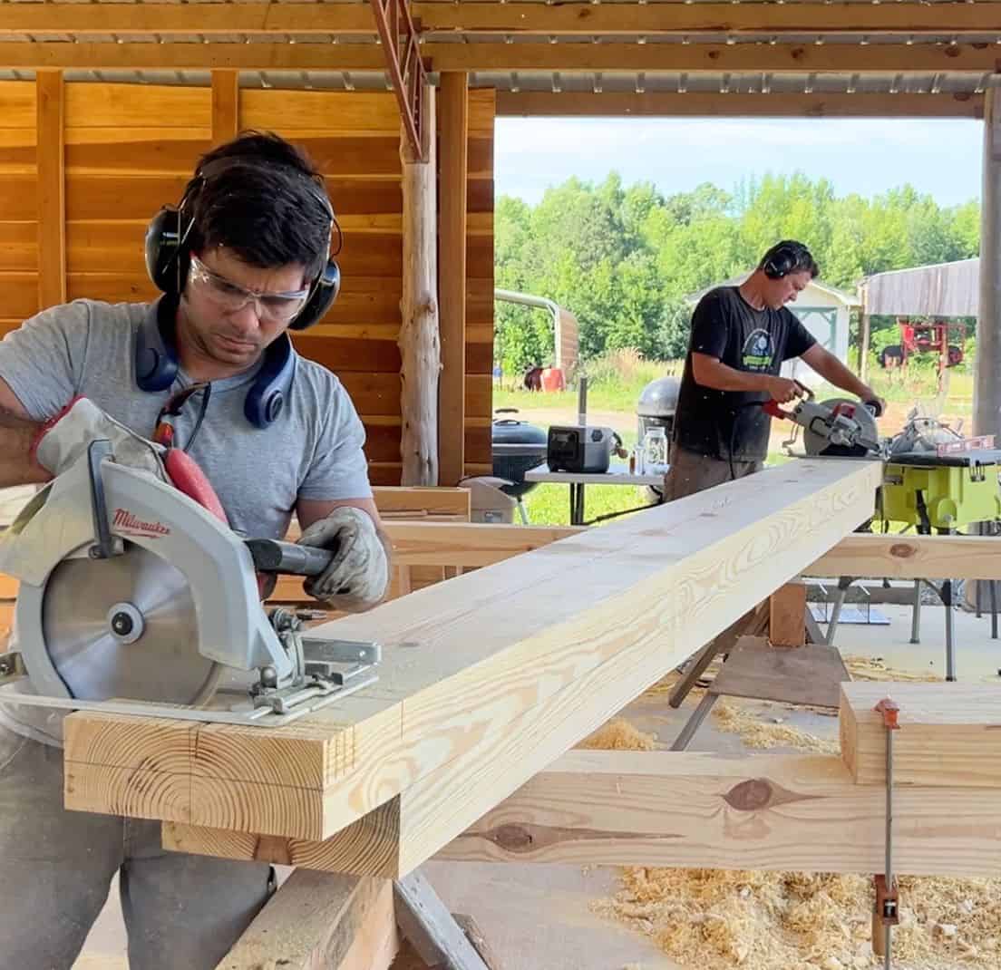 two men using circular saws to cut a beam