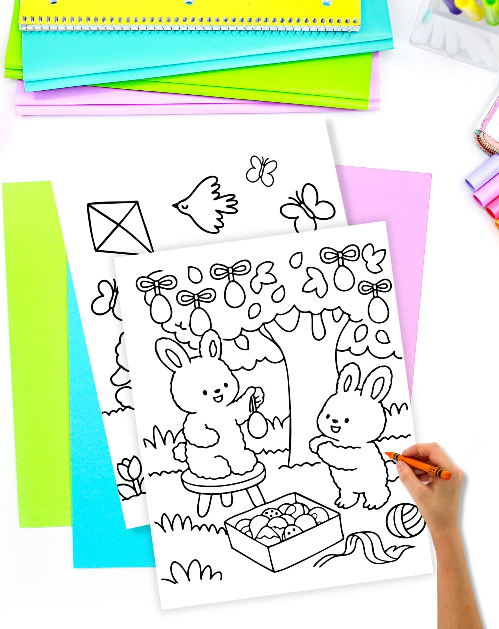 a hand with a crayon preparing to color a sheet showing bunnies decorating an Easter tree