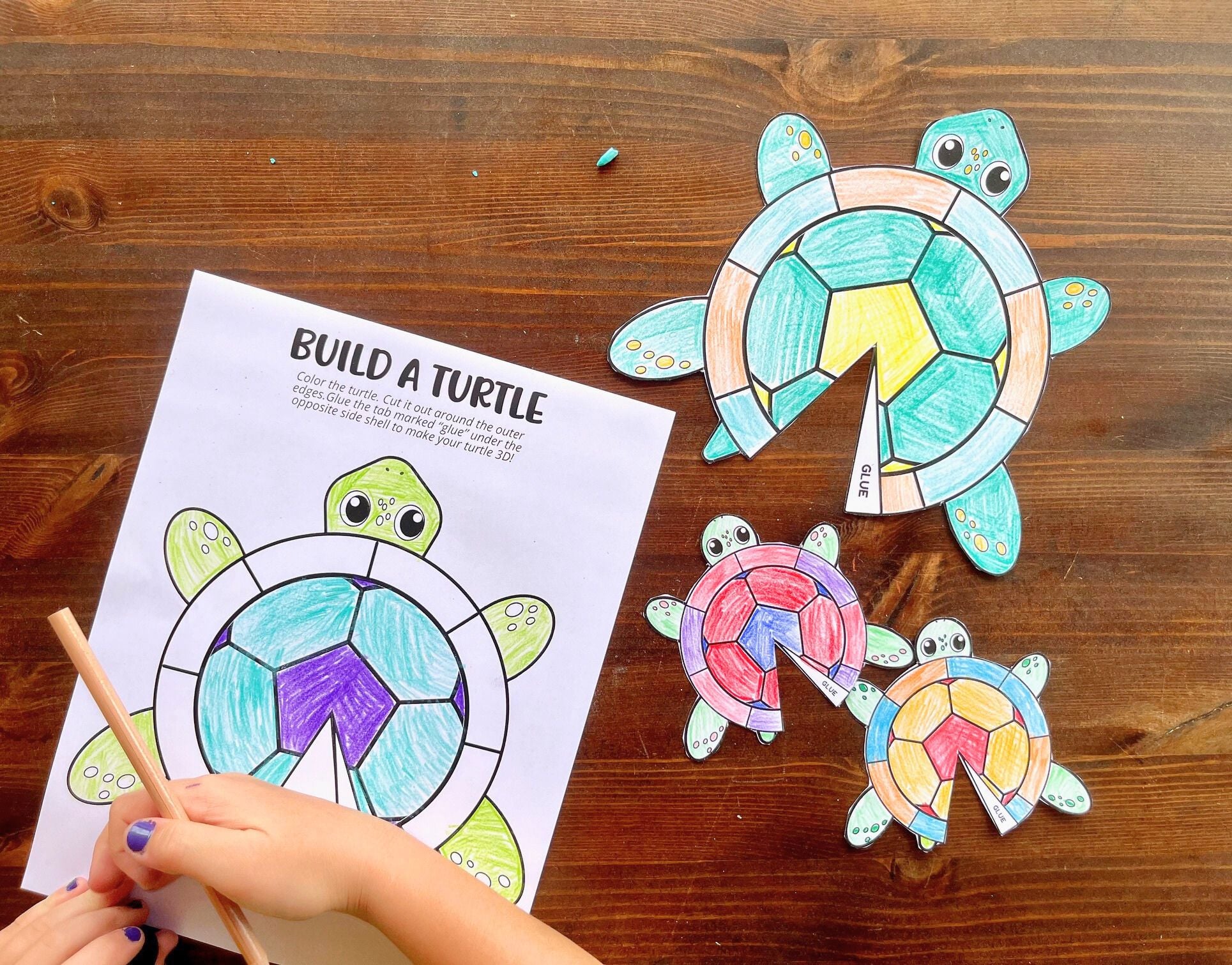 a child's hand with a colored pencil working on a paper turtle craft