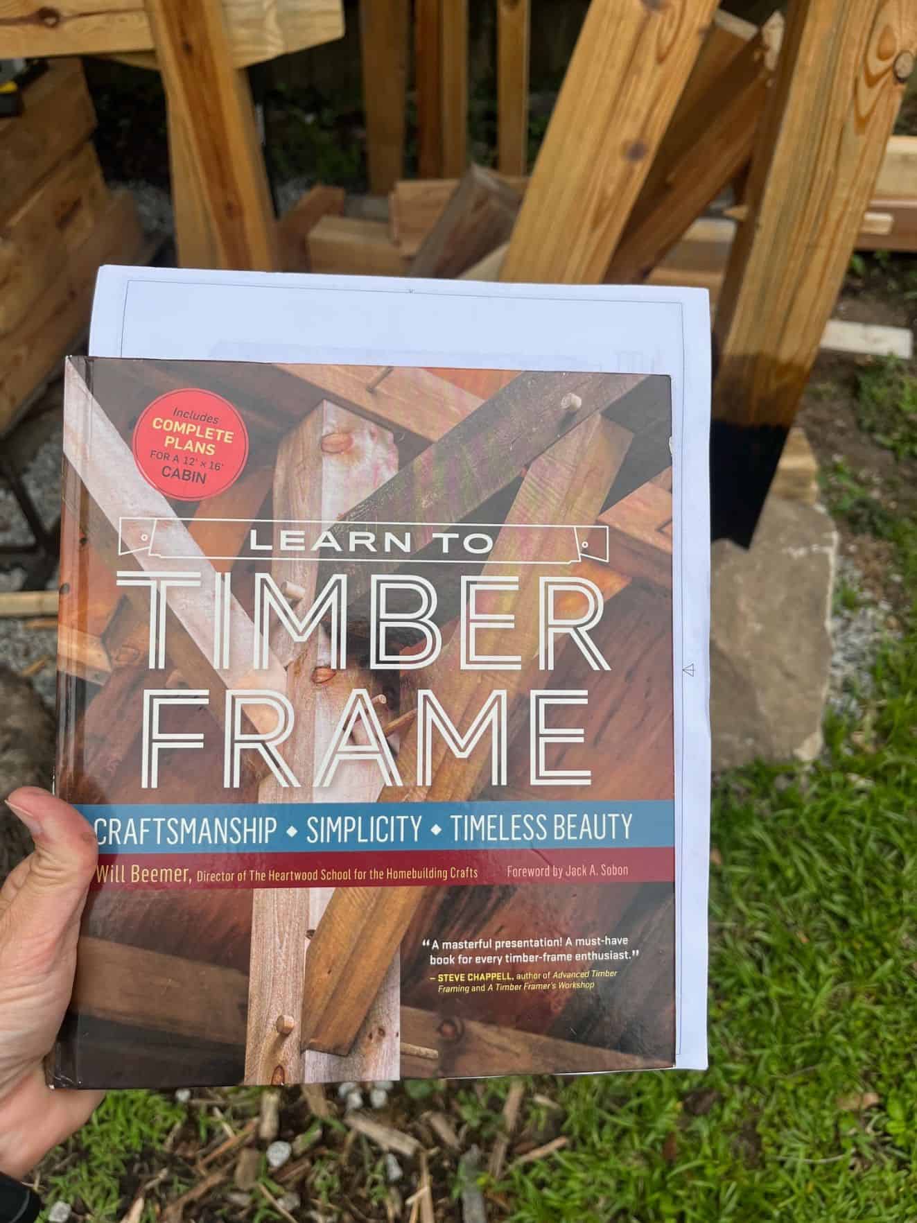 a hand holding a book called "learn to timber frame"