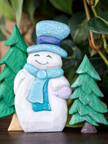 a wood carved snowman with two wood carved cristmas trees in the background