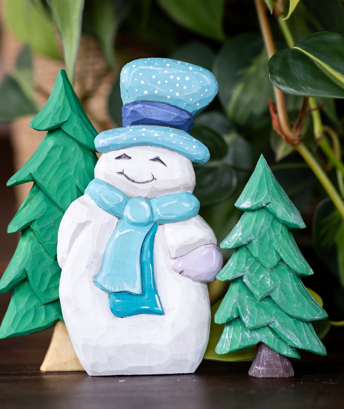 a wood carved snowman with two wood carved cristmas trees in the background