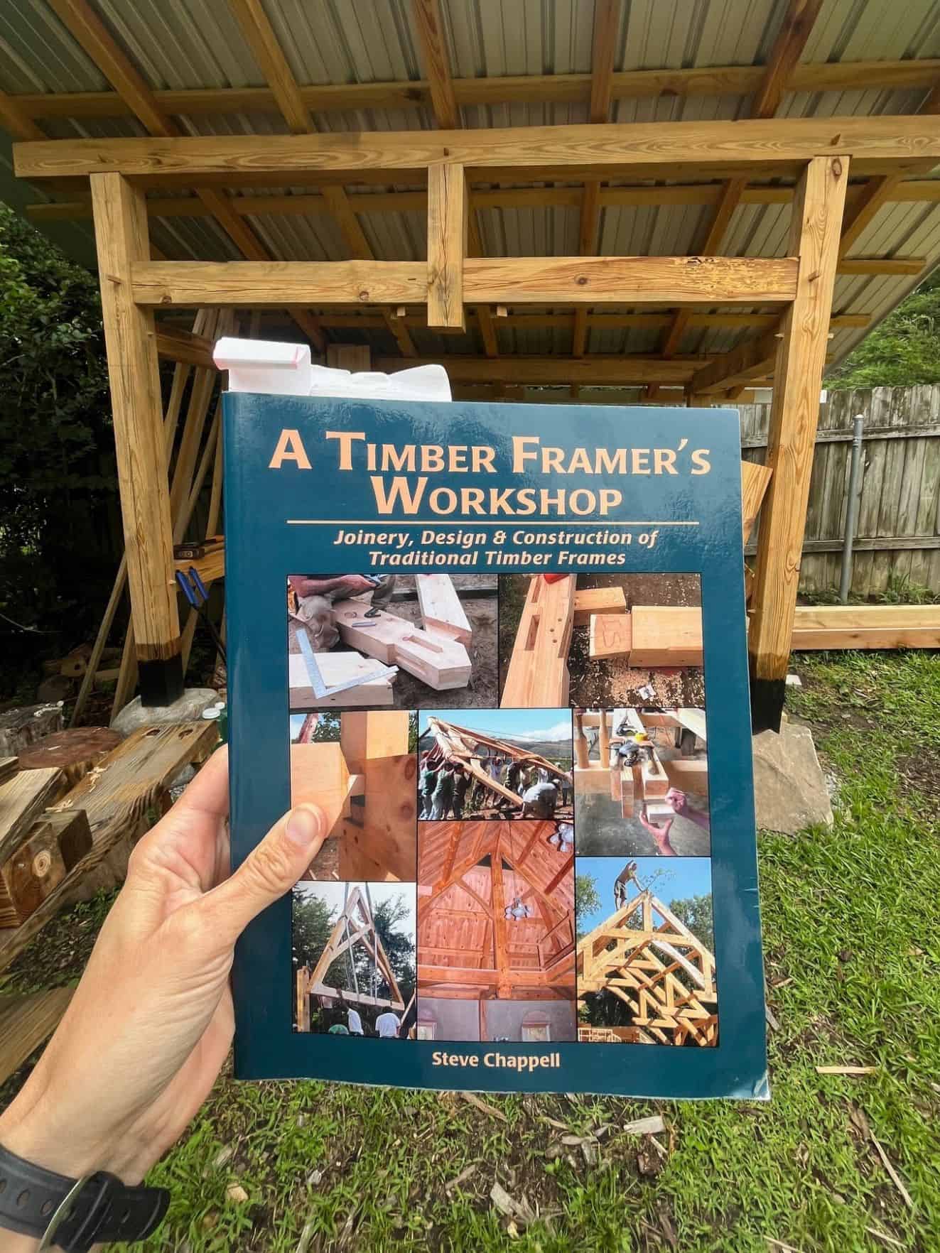 a hand holding a book called "a timber framer's workshop"