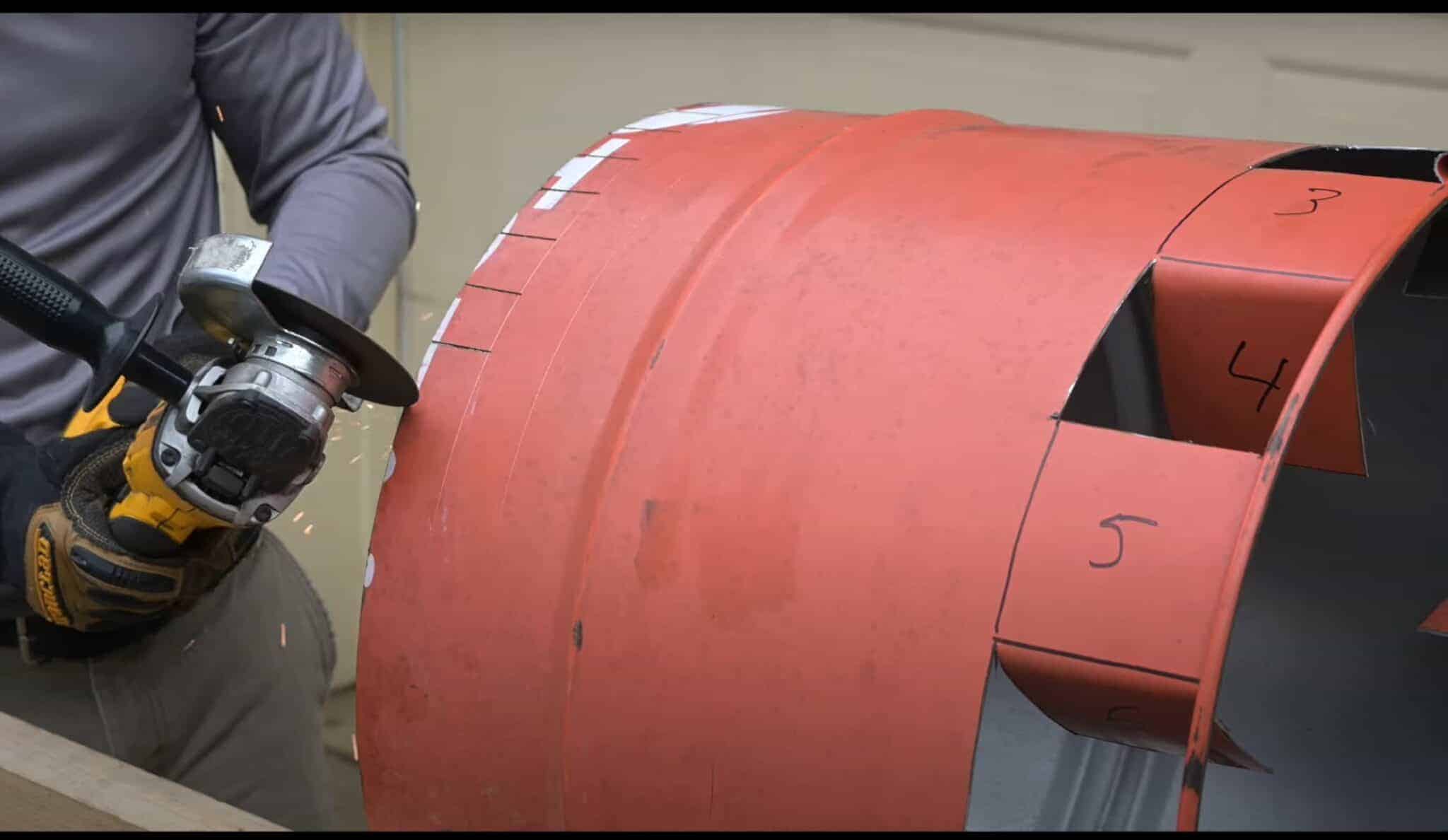 Photo is of a man cutting small tabs on a 55 gallon drum.