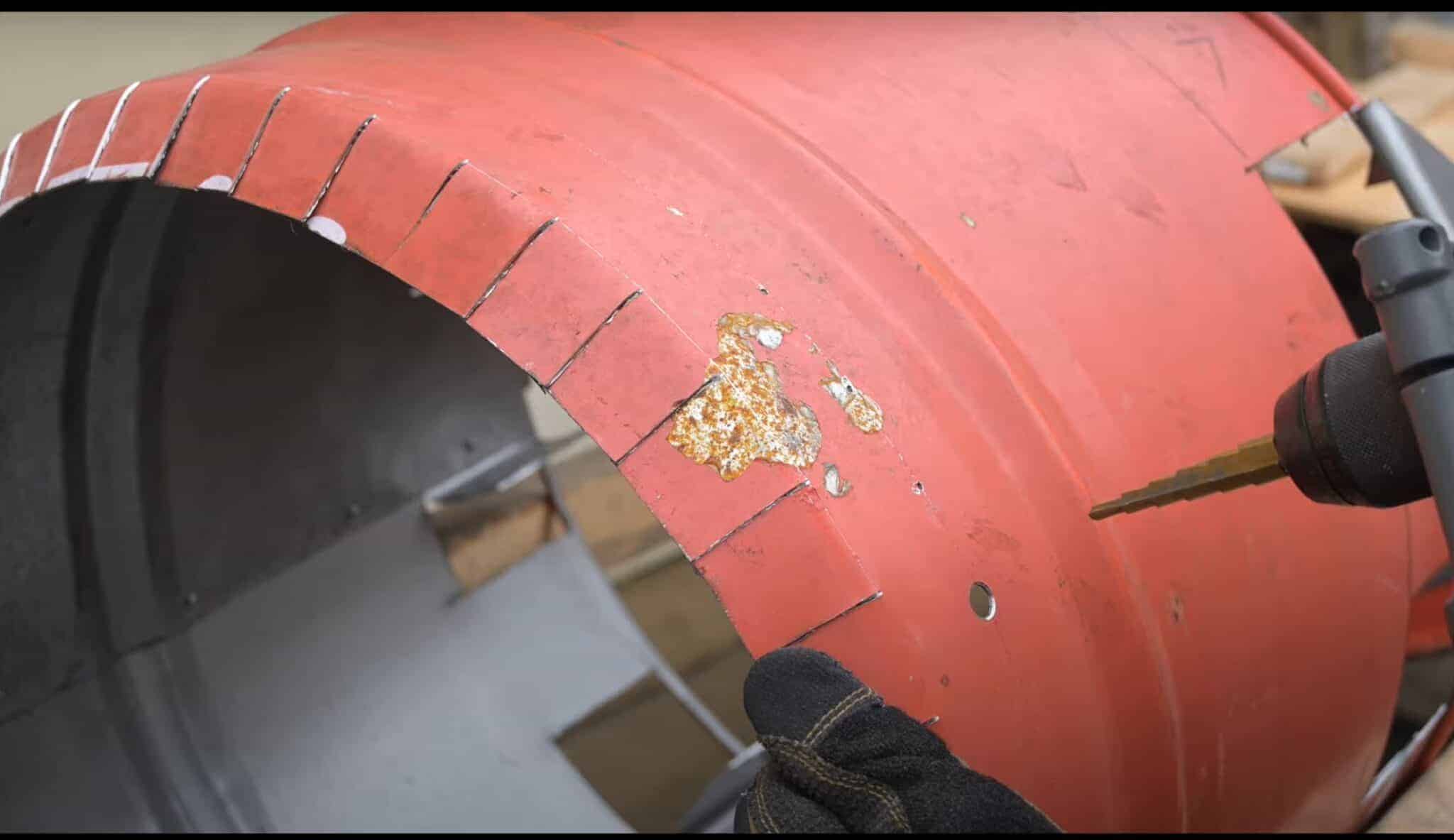 Photo is of a man drilling ½" holes into a 55 gallon drum 3 inches from the top.