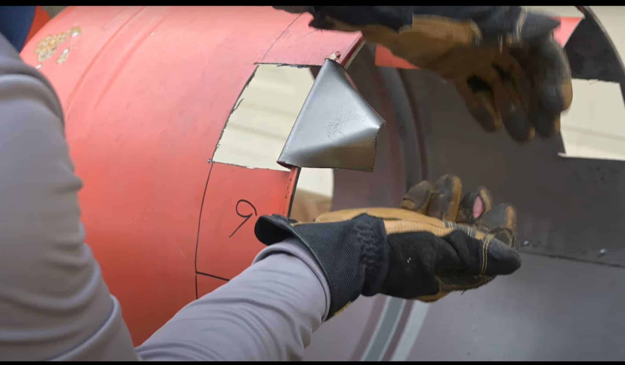 Photo is a man folding over metal cut outs of a 55 gallon drum to make legs for a firepit.