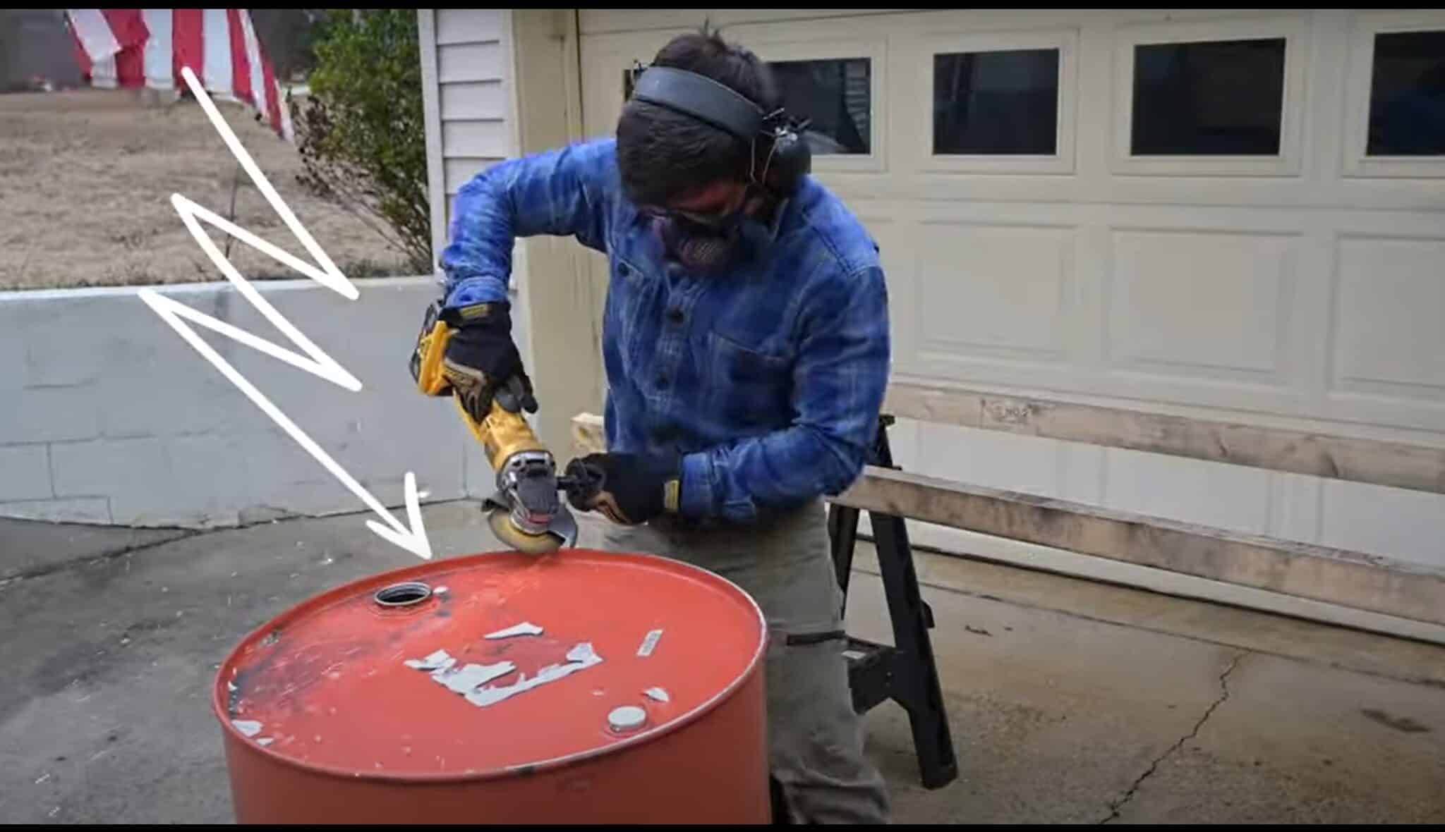 Photo is of a man grinding the top off a 55 gallon drum using a yellow Dewalt angle grinder.