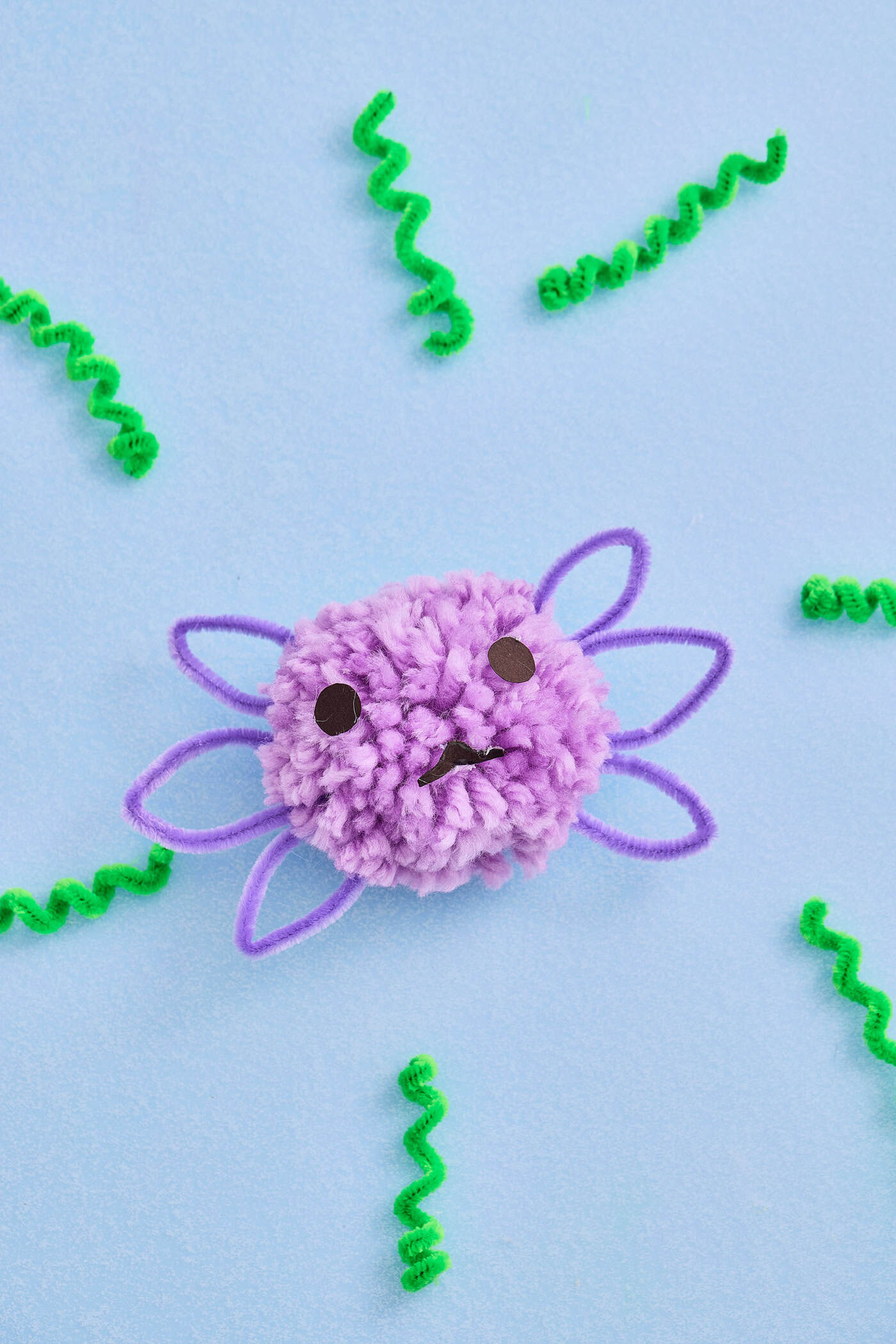 a completed cute pompom axolotl craft for kids on a blue background