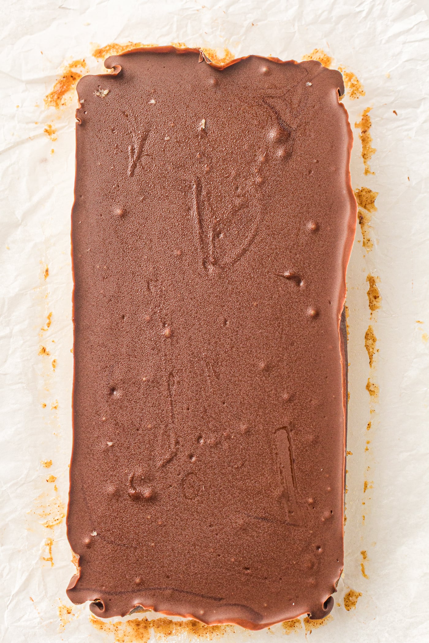 A homemade Twix bar made with almond flour, featuring a smooth chocolate topping and a base layer, is displayed on parchment paper.