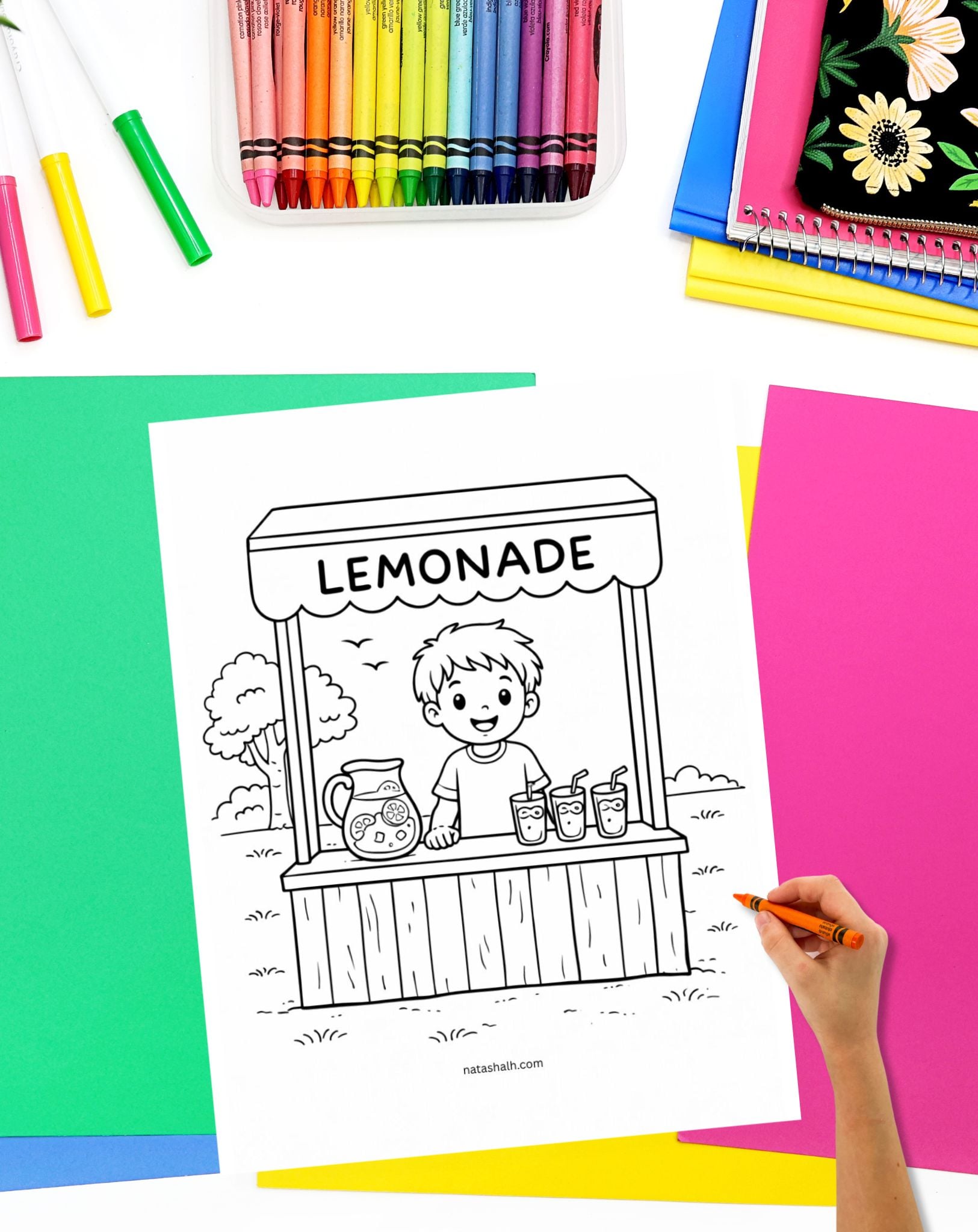 a hadn't with a crayon preparing to color a page showing a boy with a lemonade stand