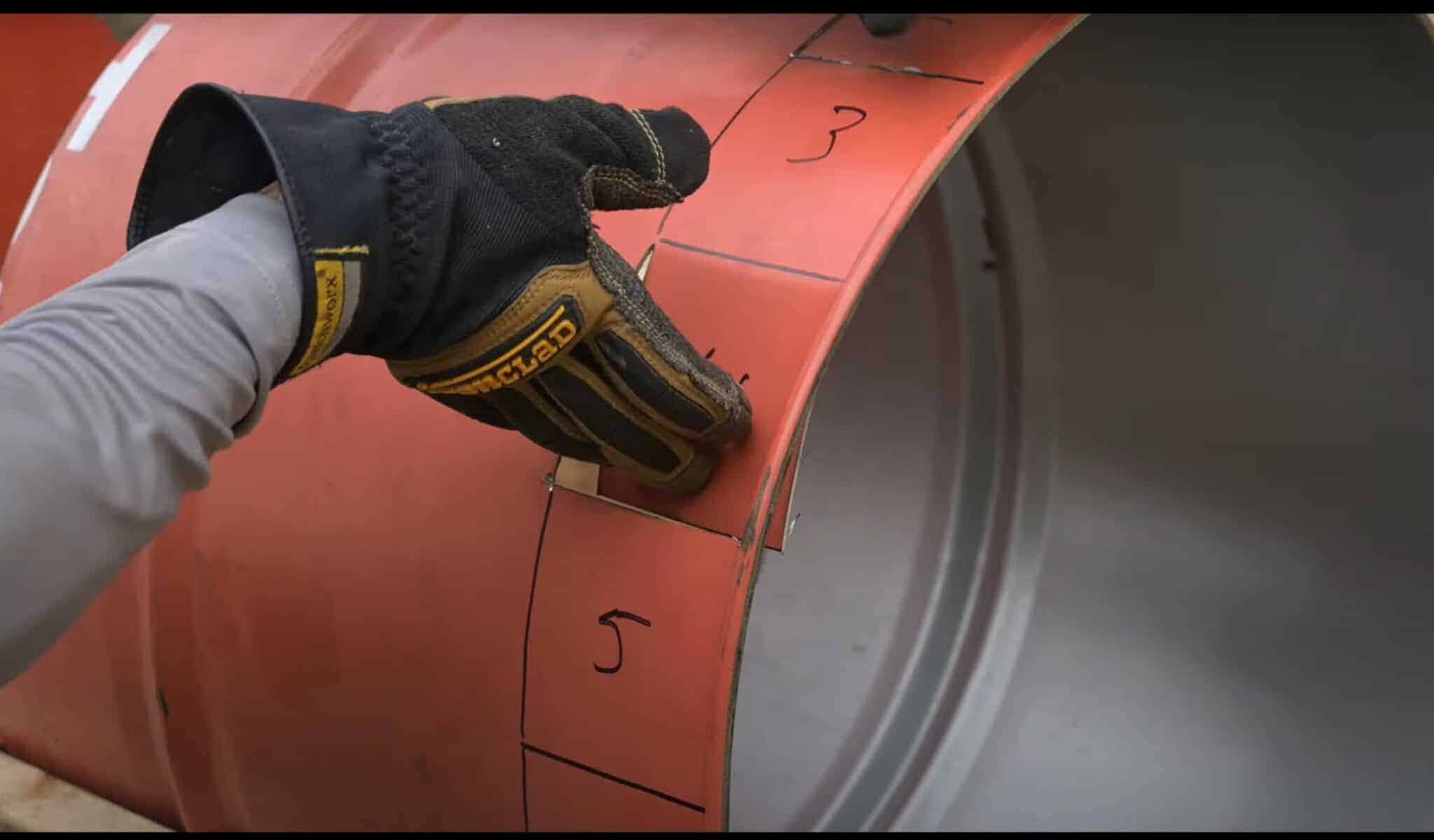 Photo is a man folding in the air vents of a 55 gallon drum for a firepit.