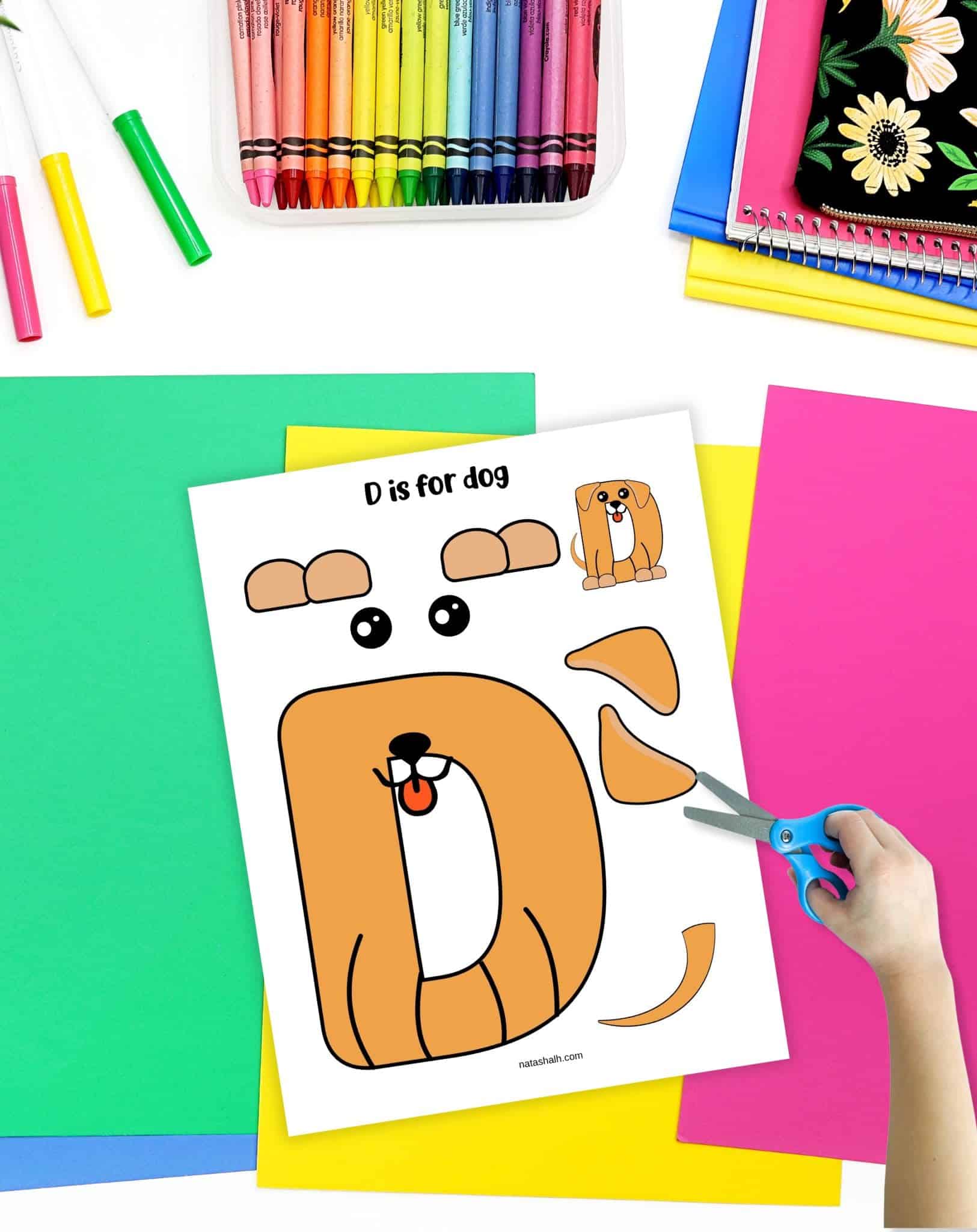 a child's hand with scissors preparing to cut out a letter d craft showing the d as a dog