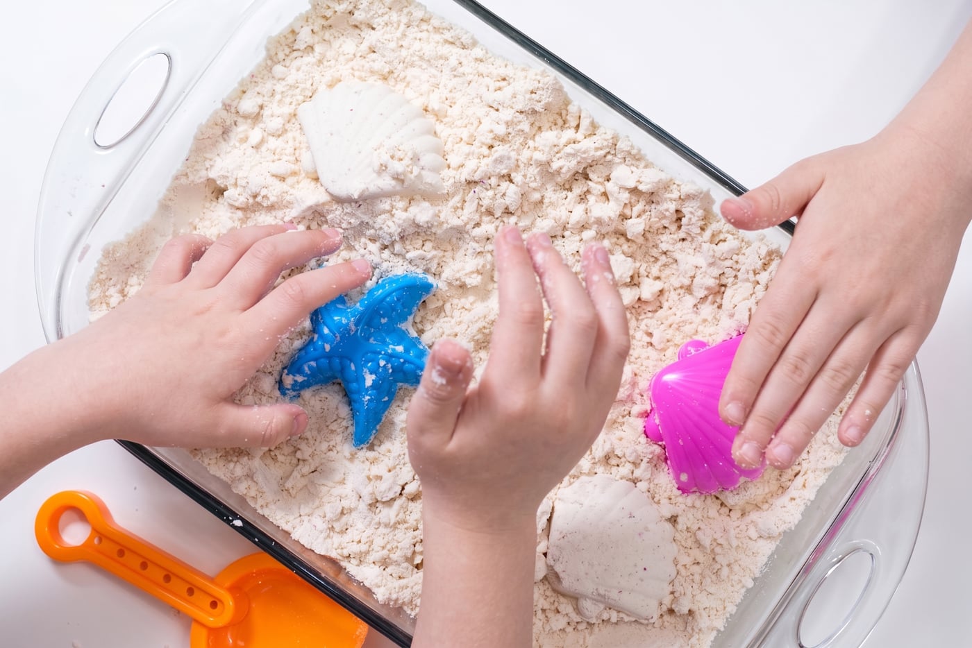 children's hands playing a dish of homemade DIY moon sand