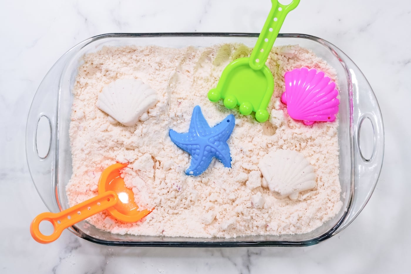 homemade kinetic sand in a dish with plastic beach toys